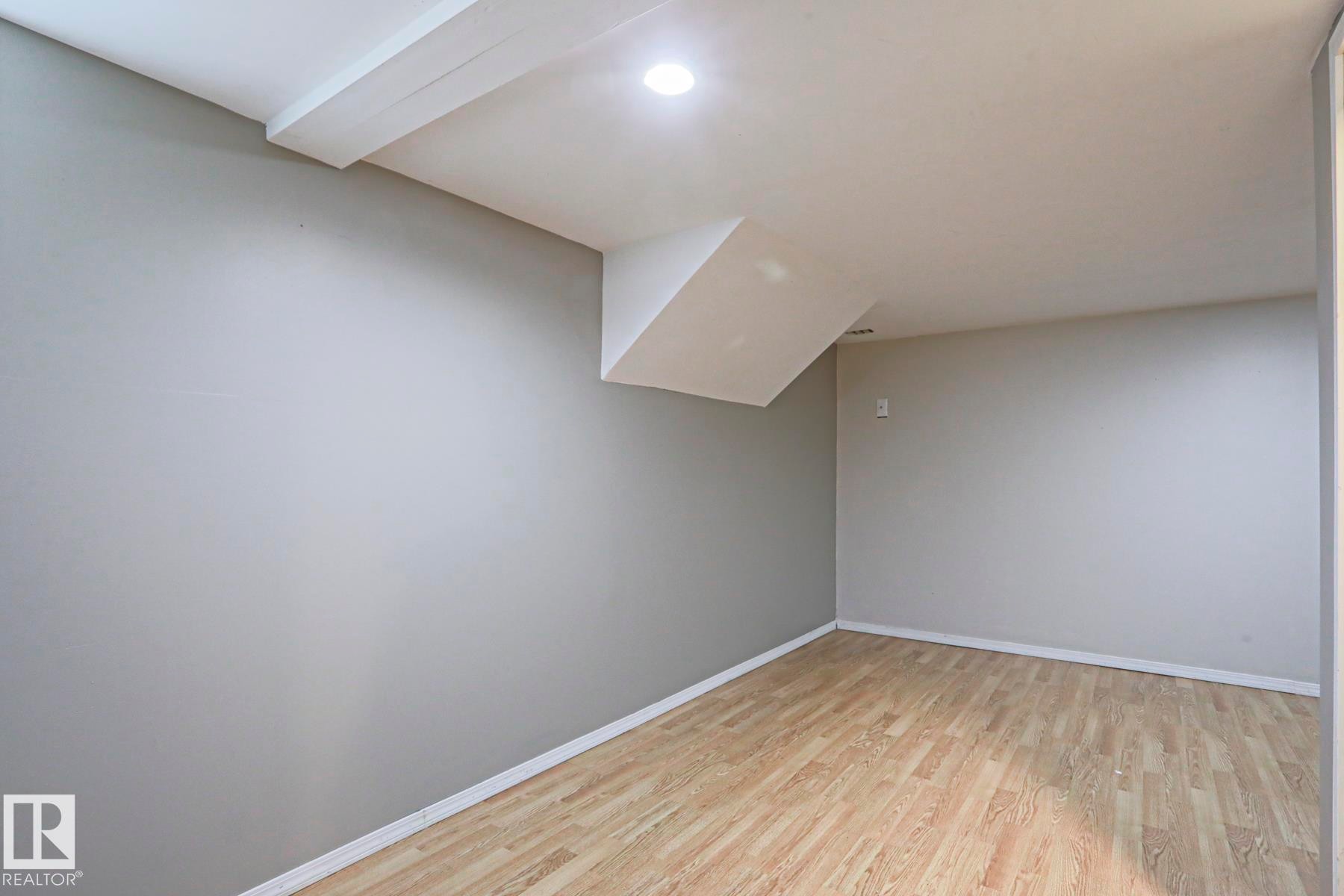 Spacious room featuring wood-finish flooring, light grey painted walls, white baseboards, a flat white ceiling, and recessed lighting - 5113 53 Avenue, Stony Plain, AB - Indoor Photo Showing Other Room