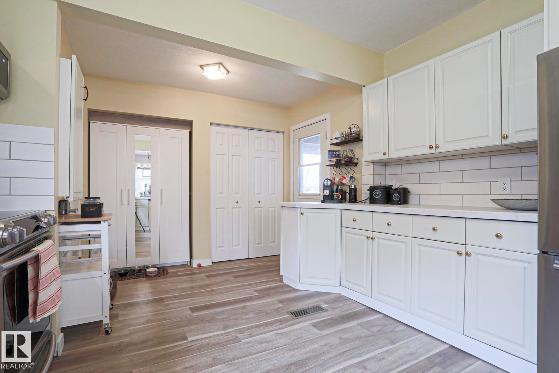 Contemporary kitchen featuring white cabinetry, subway tile backsplash, wood-finish flooring, white countertops, and stainless steel appliances - 5113 53 Avenue, Stony Plain, AB - Indoor Photo Showing Kitchen