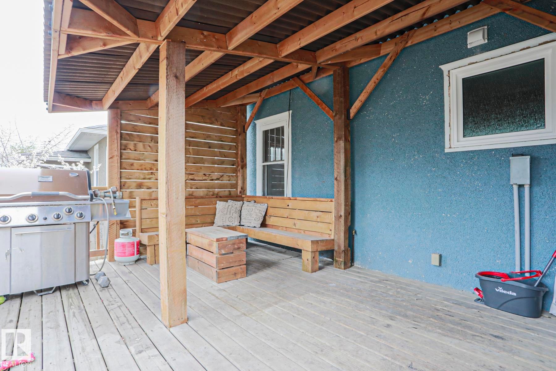 Covered outdoor deck with exposed wood beam construction, corrugated metal roofing, and built-in wood bench seating - 5113 53 Avenue, Stony Plain, AB - Outdoor With Exterior