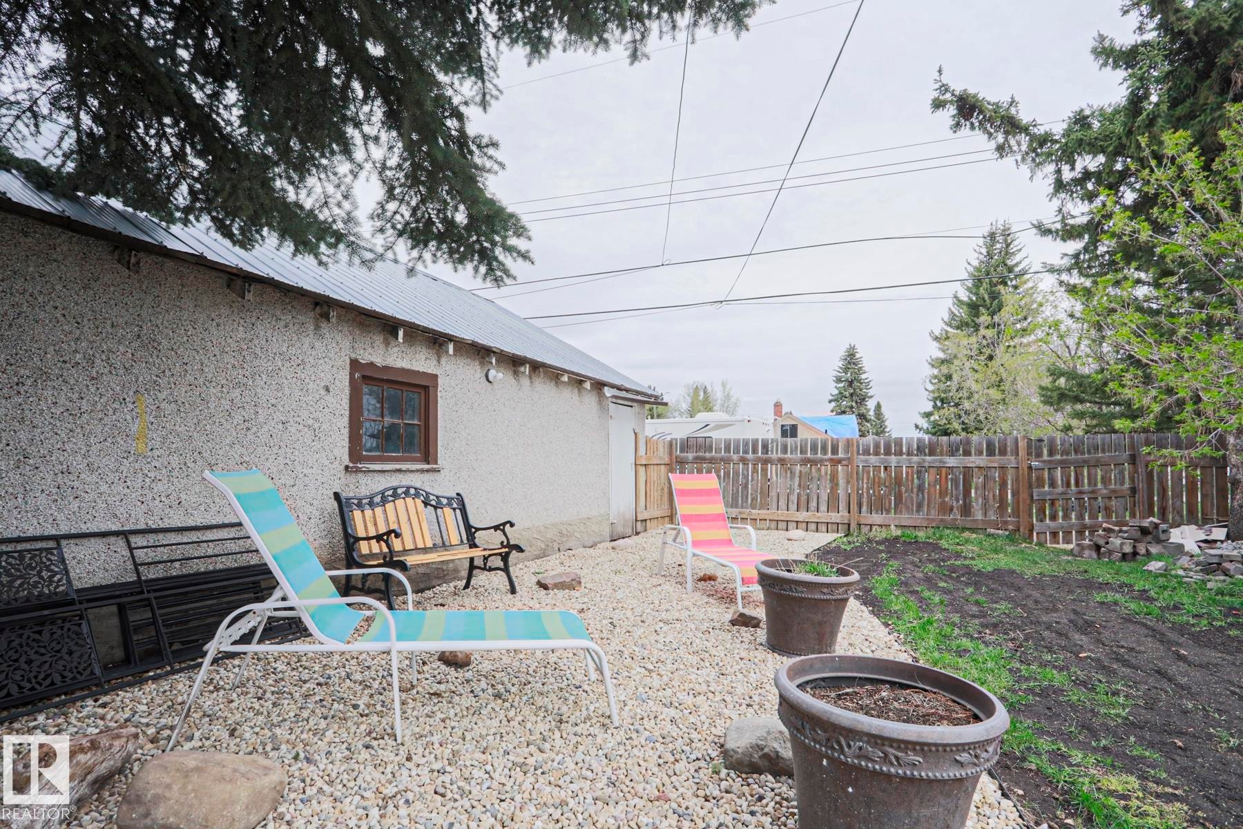 Gravel patio area featuring a stucco exterior structure with a metal roof - 5113 53 Avenue, Stony Plain, AB - Outdoor