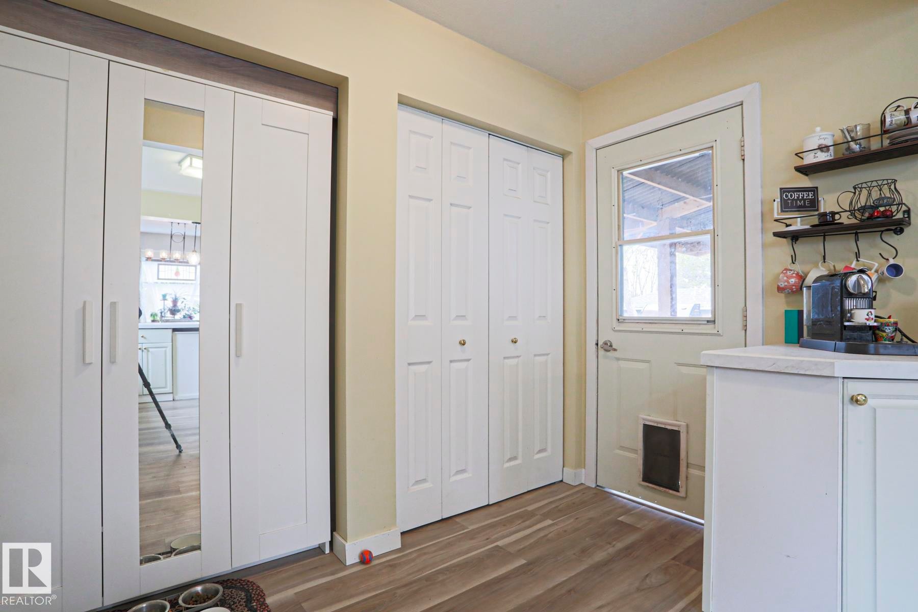 Wood-finish flooring throughout, featuring a white paneled door with glass insert, bi-fold closet doors, built-in shelving, and white cabinetry with a light-toned countertop - 5113 53 Avenue, Stony Plain, AB - Indoor Photo Showing Other Room