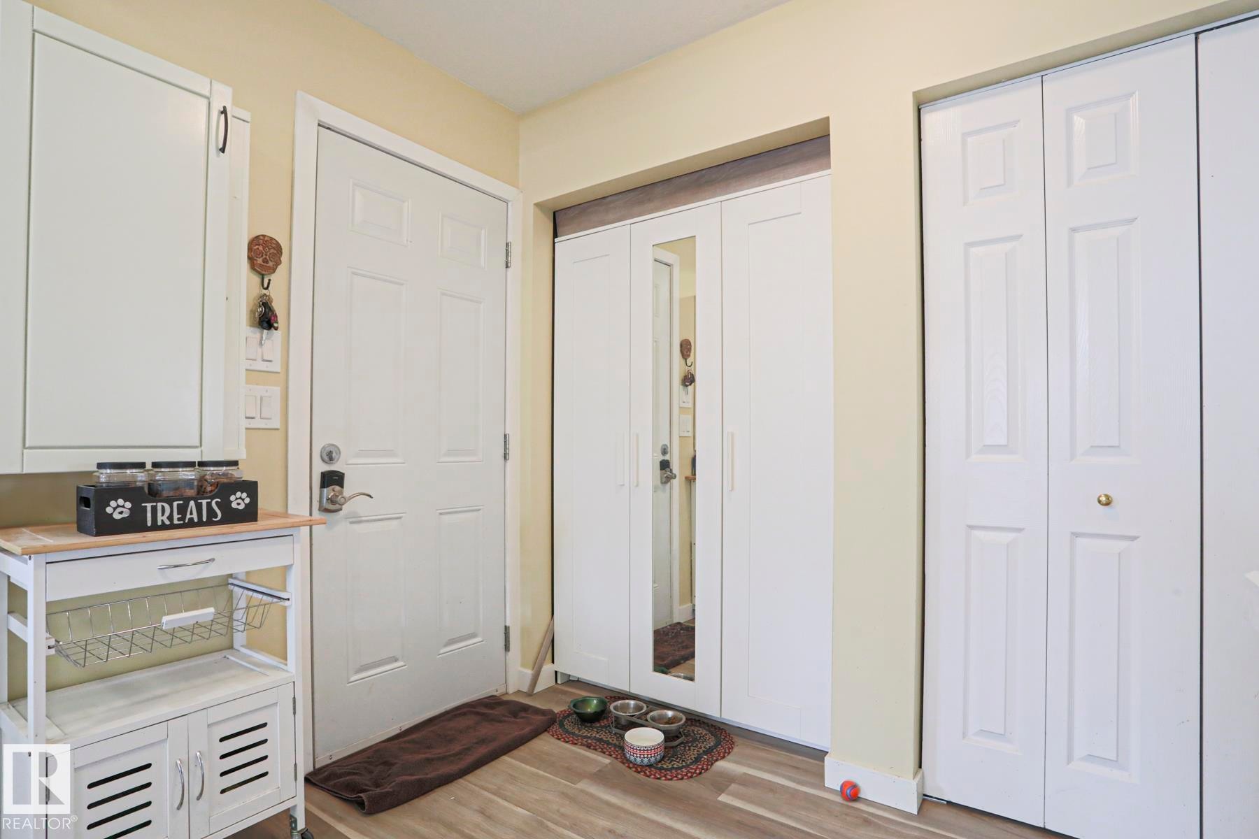 Entryway featuring wood-finish flooring, a white paneled door, and multiple storage closets with white bifold doors - 5113 53 Avenue, Stony Plain, AB - Indoor Photo Showing Other Room