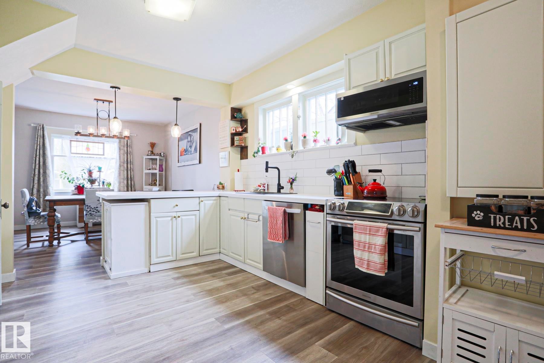 Kitchen featuring wood-finish flooring, white cabinetry, a subway tile backsplash, and stainless steel appliances - 5113 53 Avenue, Stony Plain, AB - Indoor Photo Showing Kitchen