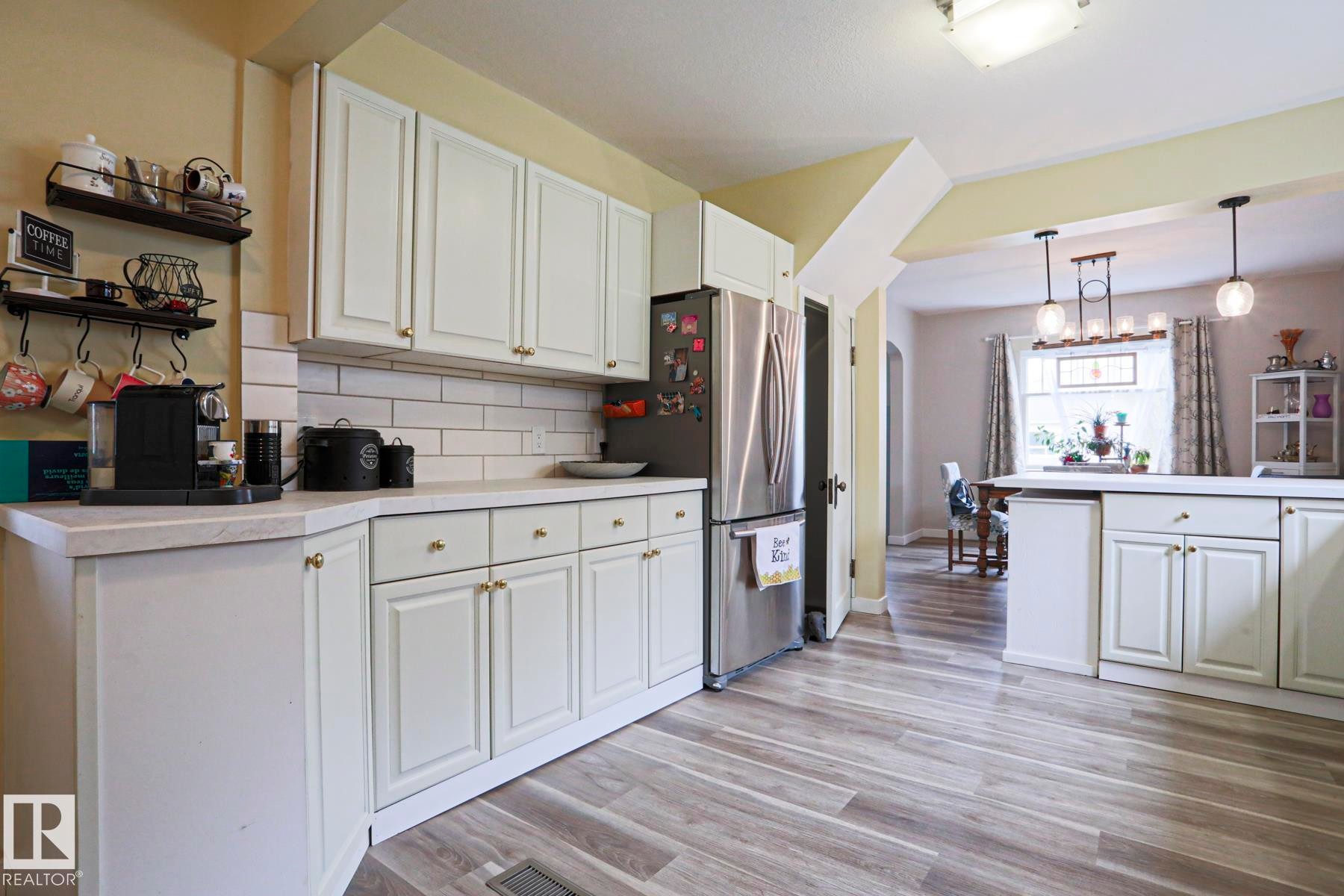 Kitchen featuring white cabinetry, light countertops, subway tile backsplash, stainless steel refrigerator, and wood-finish flooring - 5113 53 Avenue, Stony Plain, AB - Indoor Photo Showing Kitchen