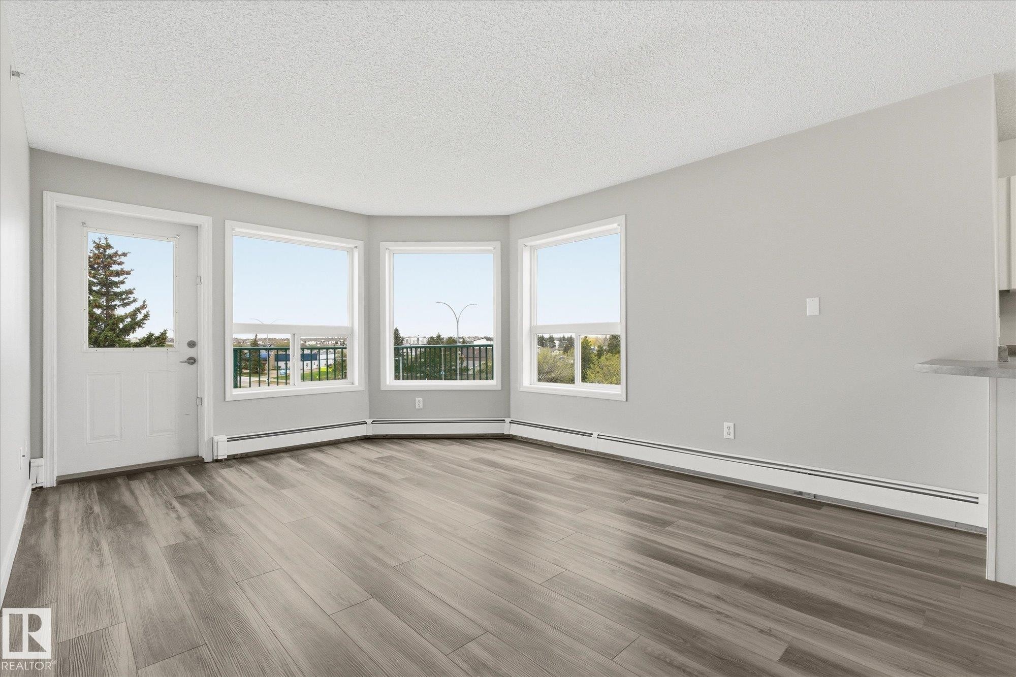 Spacious room featuring wood-finish flooring, light gray wall paint, and multiple windows - 407 13635 34 Street Nw, Edmonton, AB - Indoor