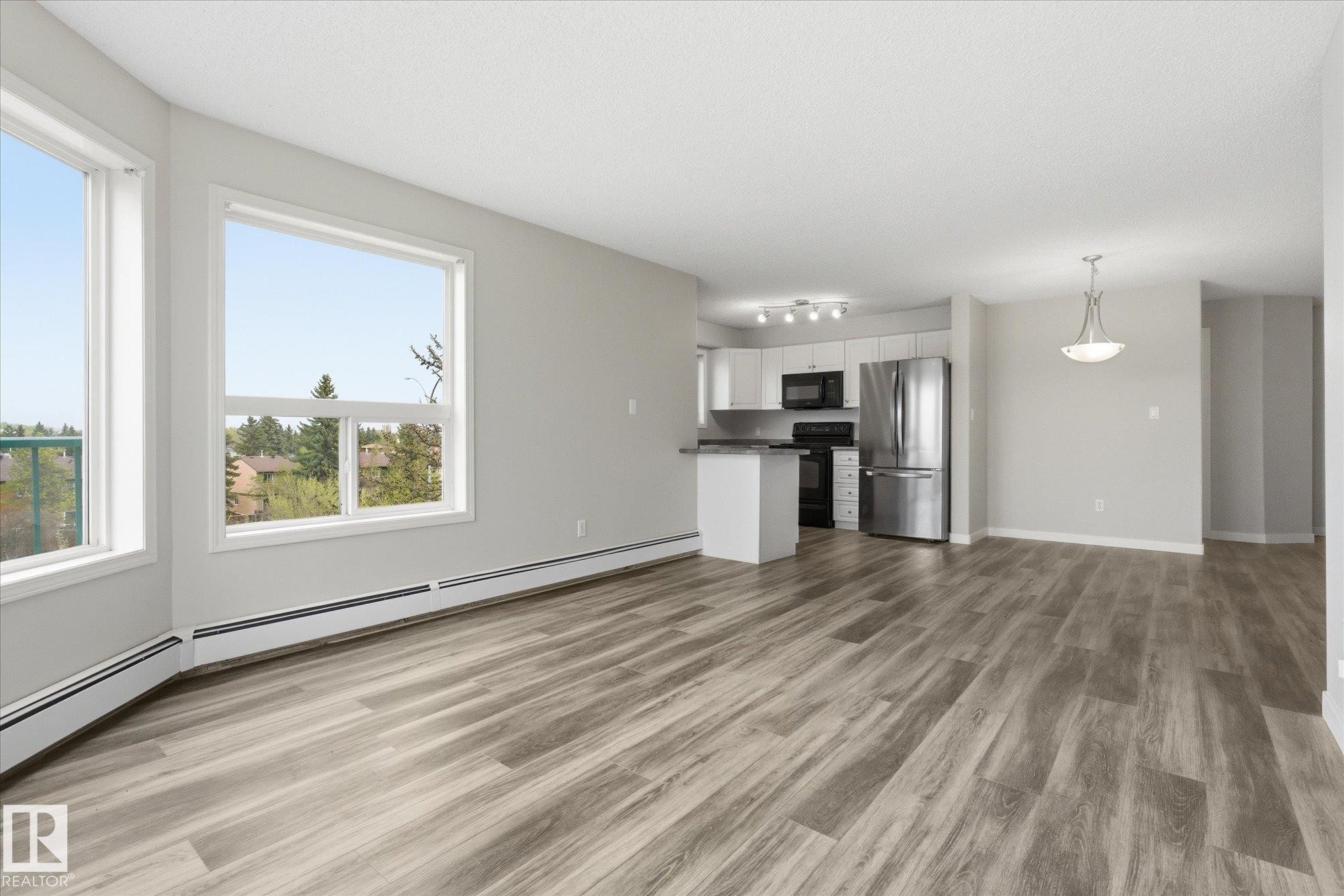 Open-concept living area featuring wood-finish flooring, large windows, recessed lighting, and a modern kitchen with stainless steel appliances - 407 13635 34 Street Nw, Edmonton, AB - Indoor Photo Showing Other Room