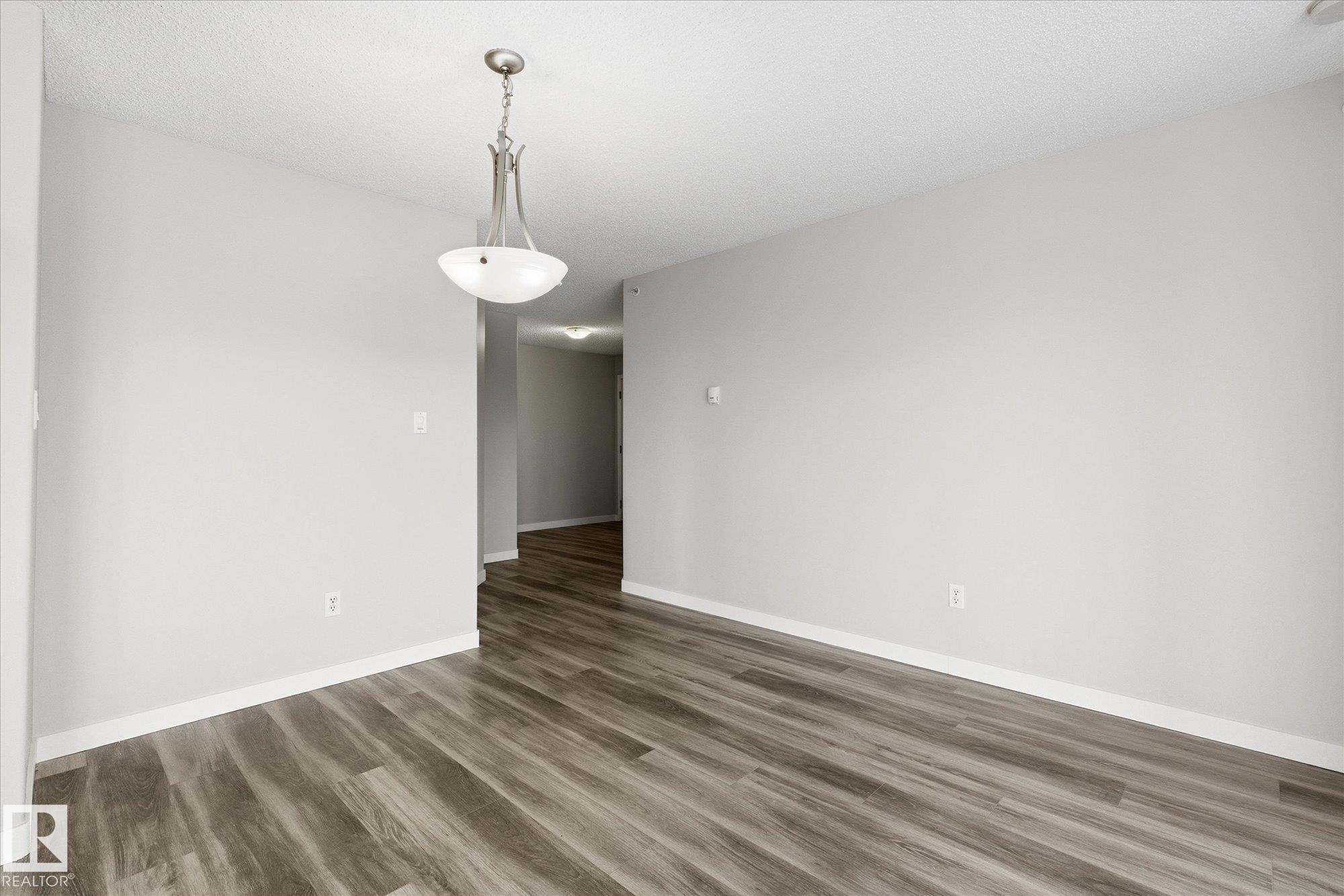 Spacious room featuring wood-finish flooring, light grey painted walls, white baseboards, and a textured ceiling - 407 13635 34 Street Nw, Edmonton, AB - Indoor Photo Showing Other Room