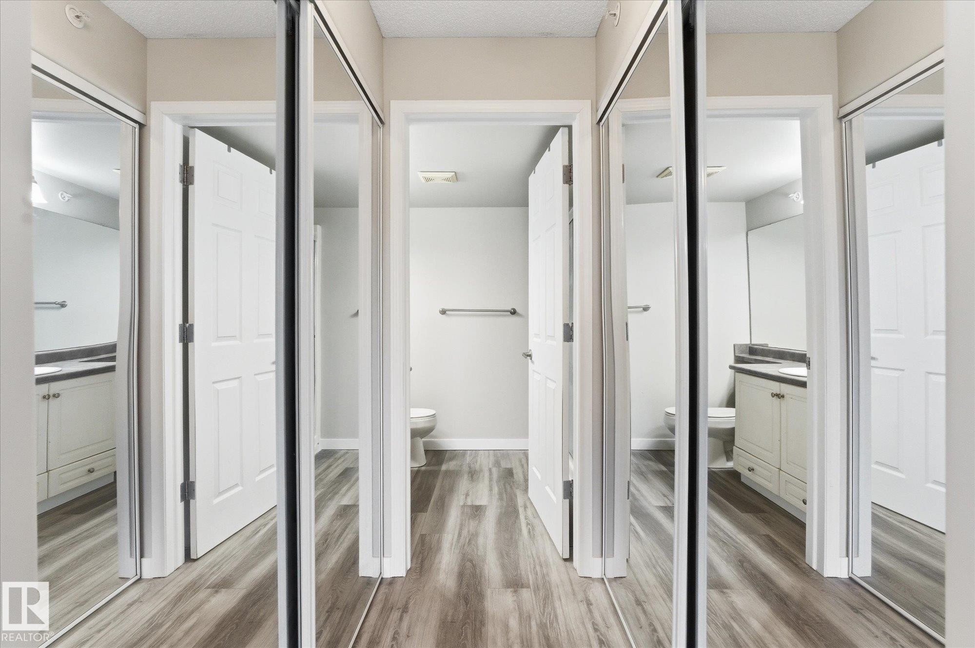 Hallway featuring wood-finish flooring, mirrored closet doors, and recessed lighting - 407 13635 34 Street Nw, Edmonton, AB - Indoor