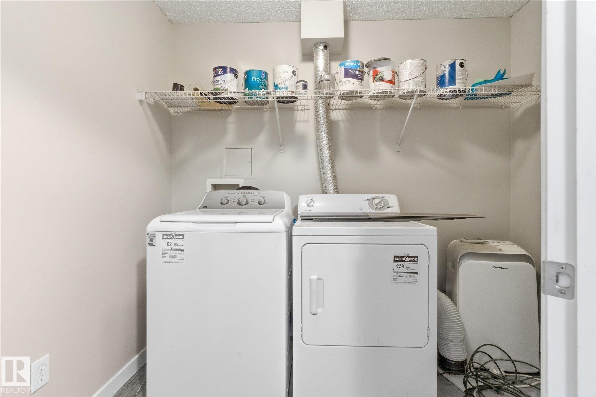 Dedicated laundry area featuring a wire rack shelf for storage, neutral wall paint, and wood-finish flooring - 407 13635 34 Street Nw, Edmonton, AB - Indoor Photo Showing Laundry Room