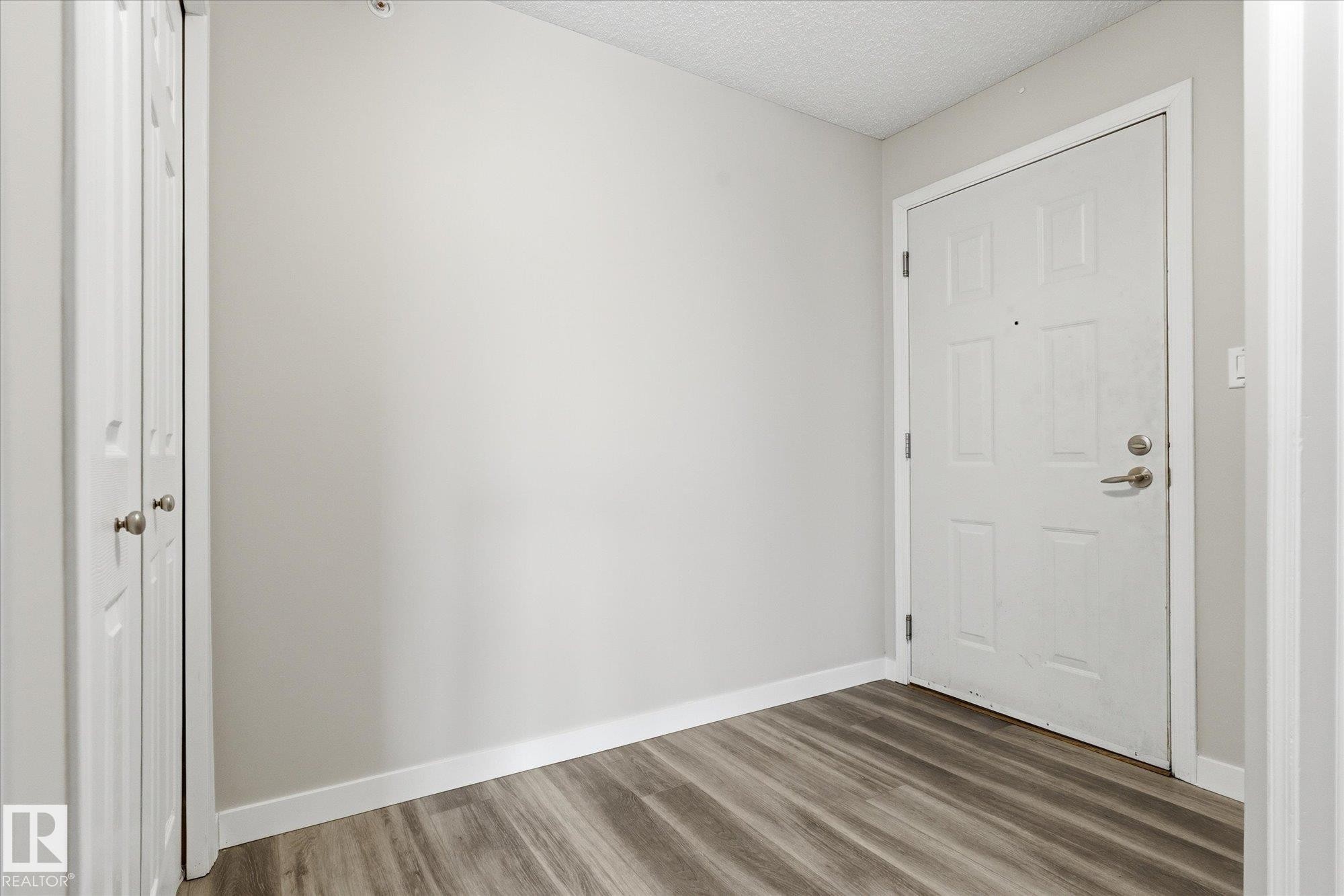 Entryway featuring wood-finish flooring, light gray wall paint, and white baseboards - 407 13635 34 Street Nw, Edmonton, AB - Indoor Photo Showing Other Room