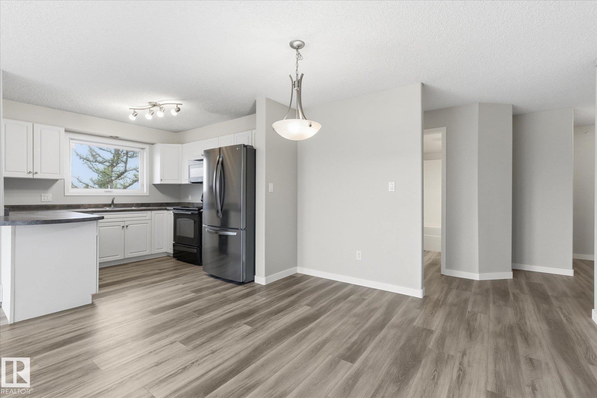 Open-concept kitchen and dining area featuring wood-finish flooring, white cabinetry, dark countertops, and stainless steel appliances - 407 13635 34 Street Nw, Edmonton, AB - Indoor Photo Showing Kitchen