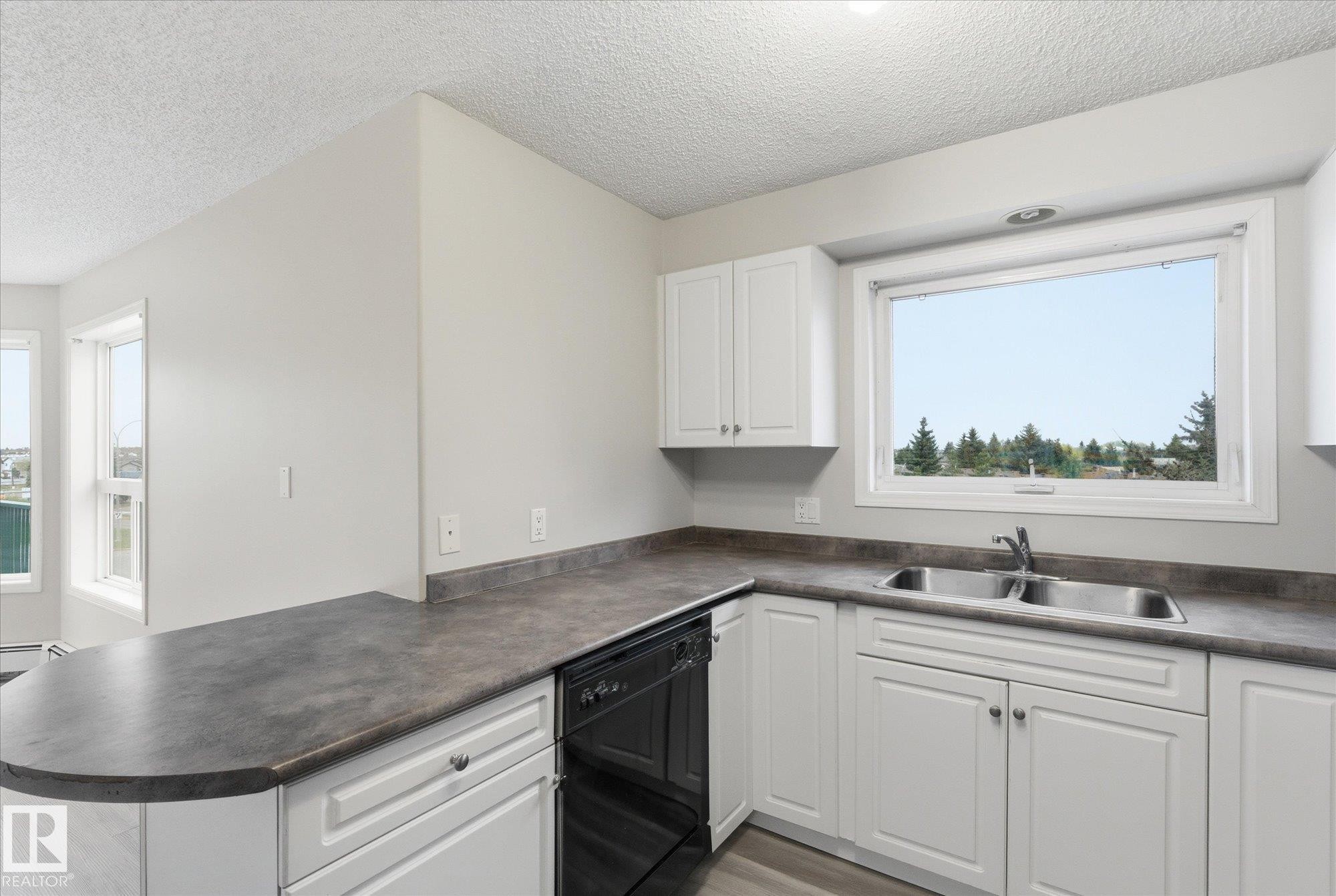 Kitchen featuring white cabinetry, gray countertops, a double basin stainless steel sink, and a black dishwasher - 407 13635 34 Street Nw, Edmonton, AB - Indoor Photo Showing Kitchen With Double Sink