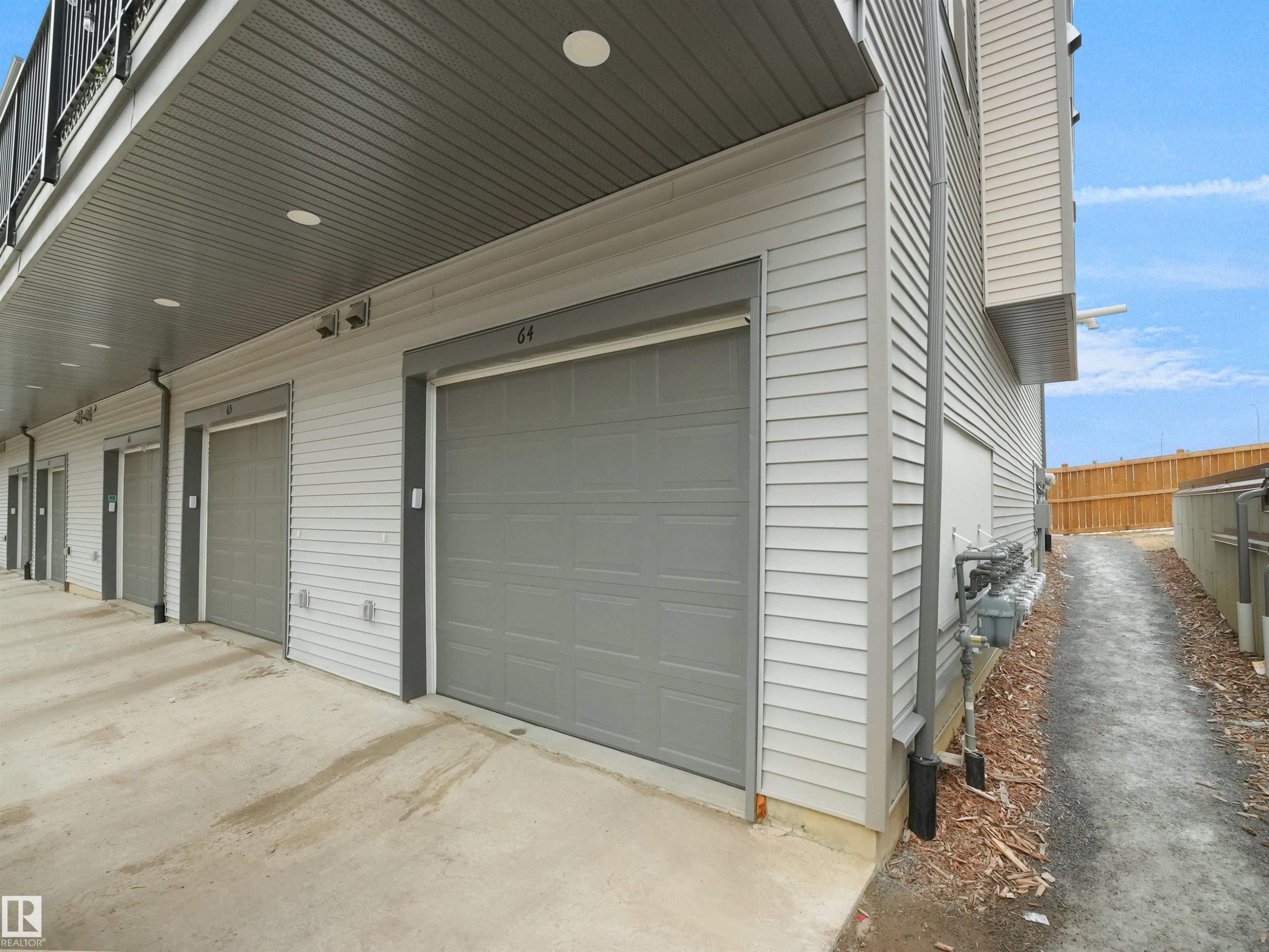 The property features an exterior with light-colored siding and gray garage doors - 64 655 Watt Boulevard, Edmonton, AB - Outdoor With Exterior