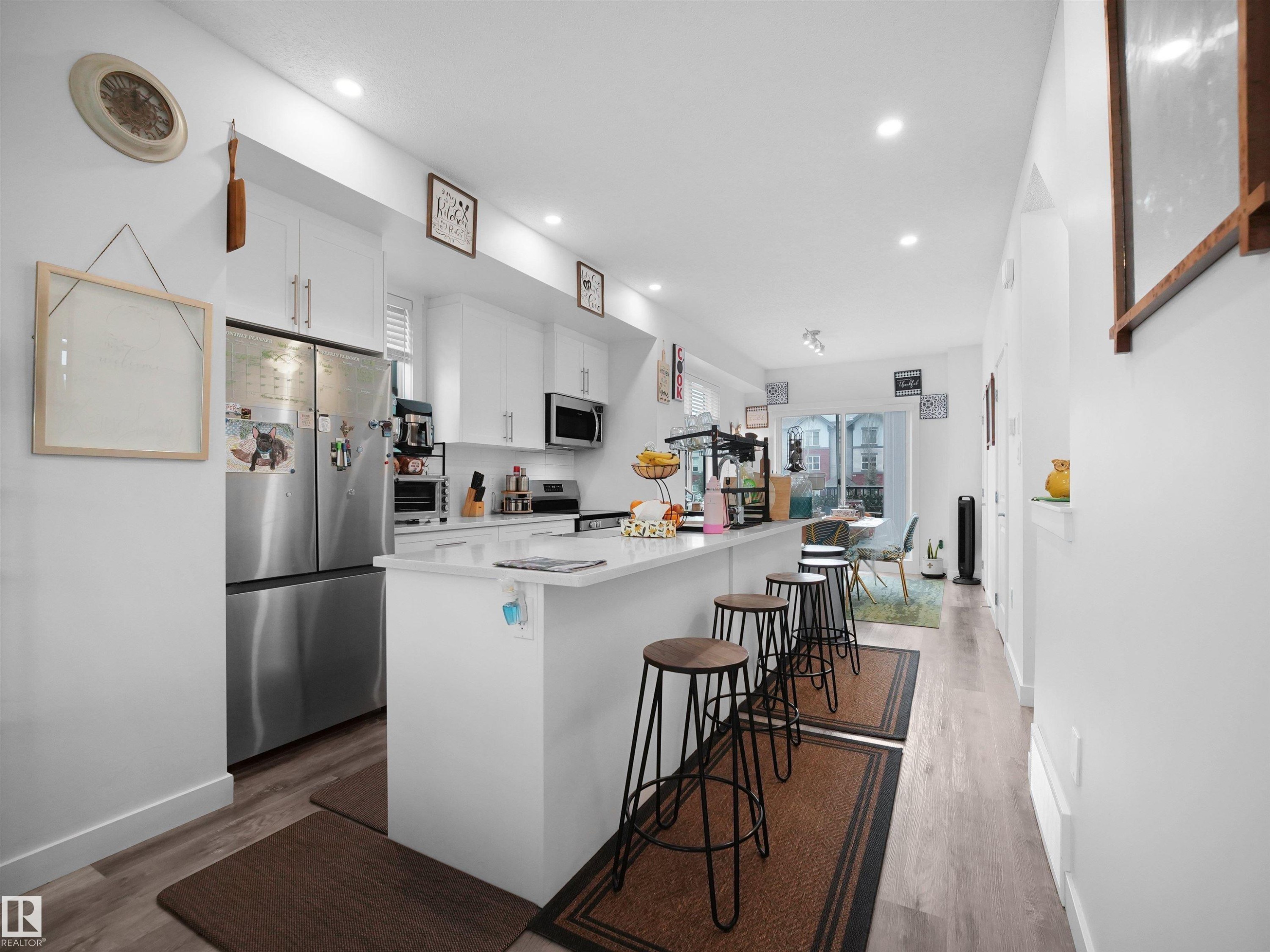 The kitchen features white cabinetry, stainless steel appliances, and a central island with a light-colored countertop - 64 655 Watt Boulevard, Edmonton, AB - Indoor Photo Showing Kitchen With Upgraded Kitchen
