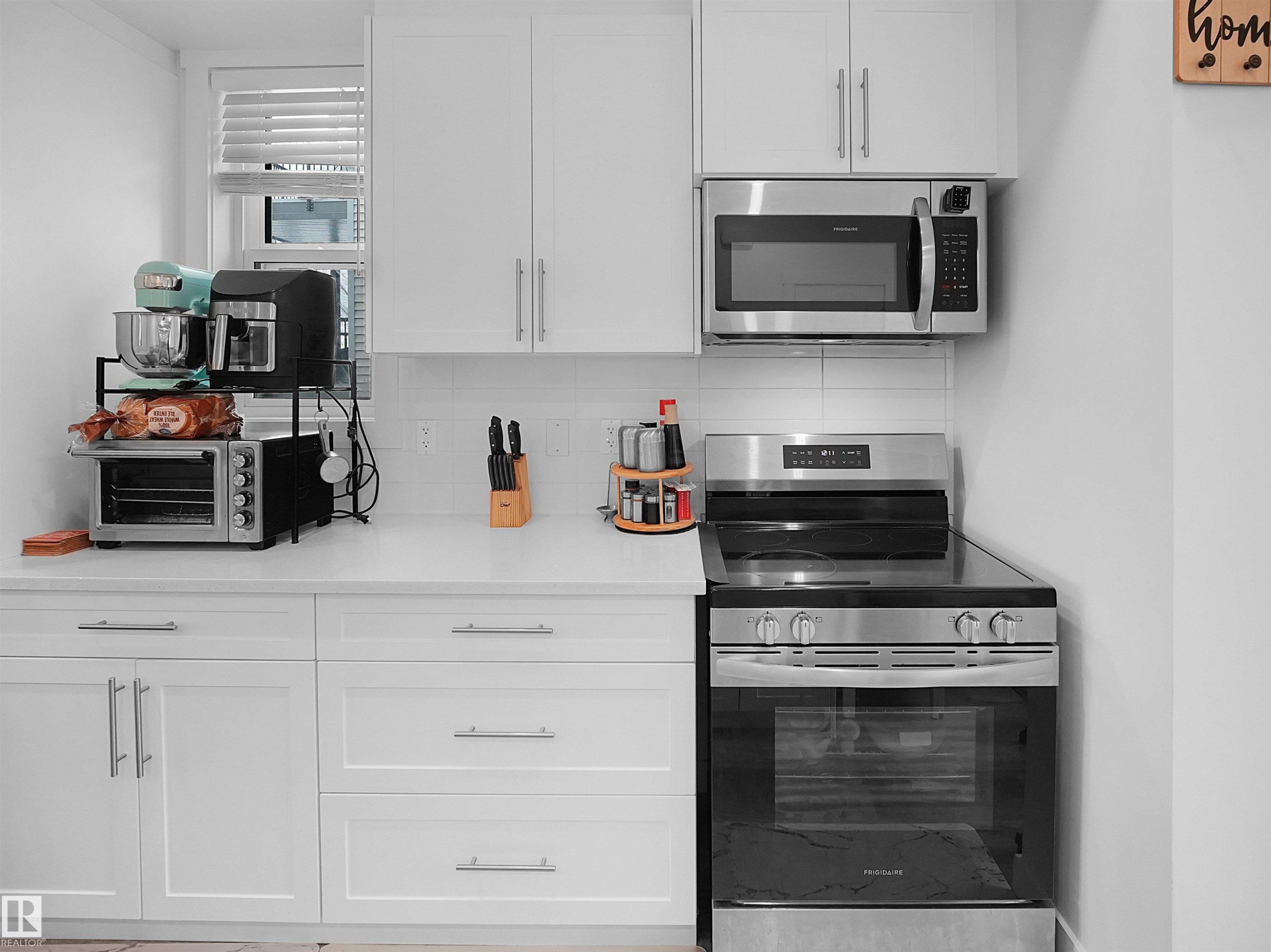 The kitchen features white cabinetry, a white countertop, a white tiled backsplash, and stainless steel appliances including a microwave and a range - 64 655 Watt Boulevard, Edmonton, AB - Indoor Photo Showing Kitchen