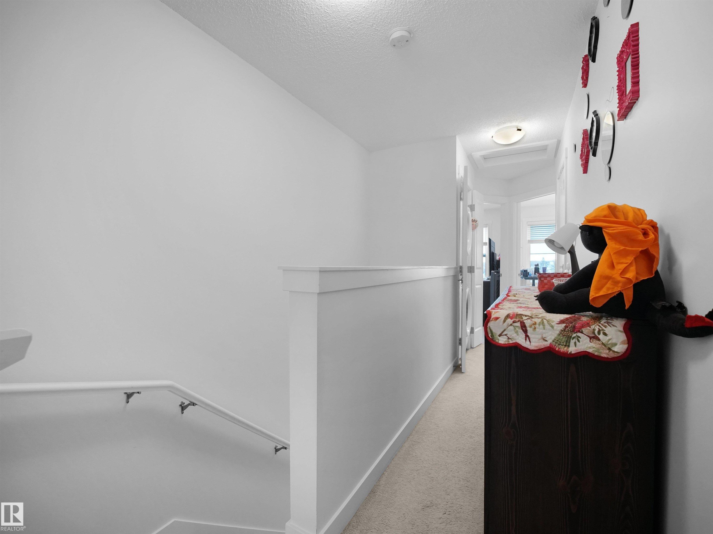 Well-lit hallway with white walls and a carpeted floor, featuring a white handrail and trim - 64 655 Watt Boulevard, Edmonton, AB - Indoor Photo Showing Other Room