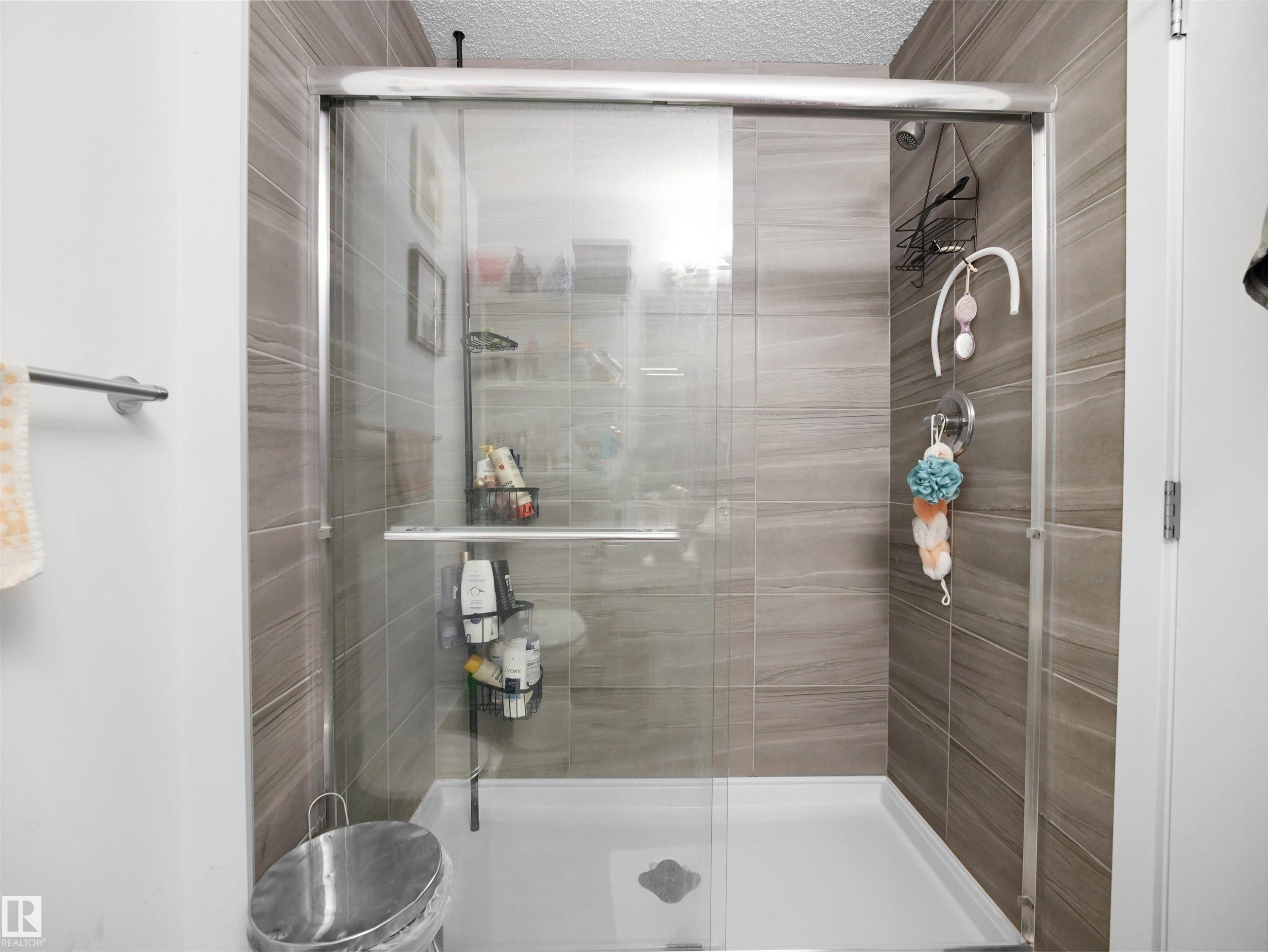 The bathroom features a shower with sliding glass doors, a white shower base, and light brown tiled walls - 64 655 Watt Boulevard, Edmonton, AB - Indoor Photo Showing Bathroom