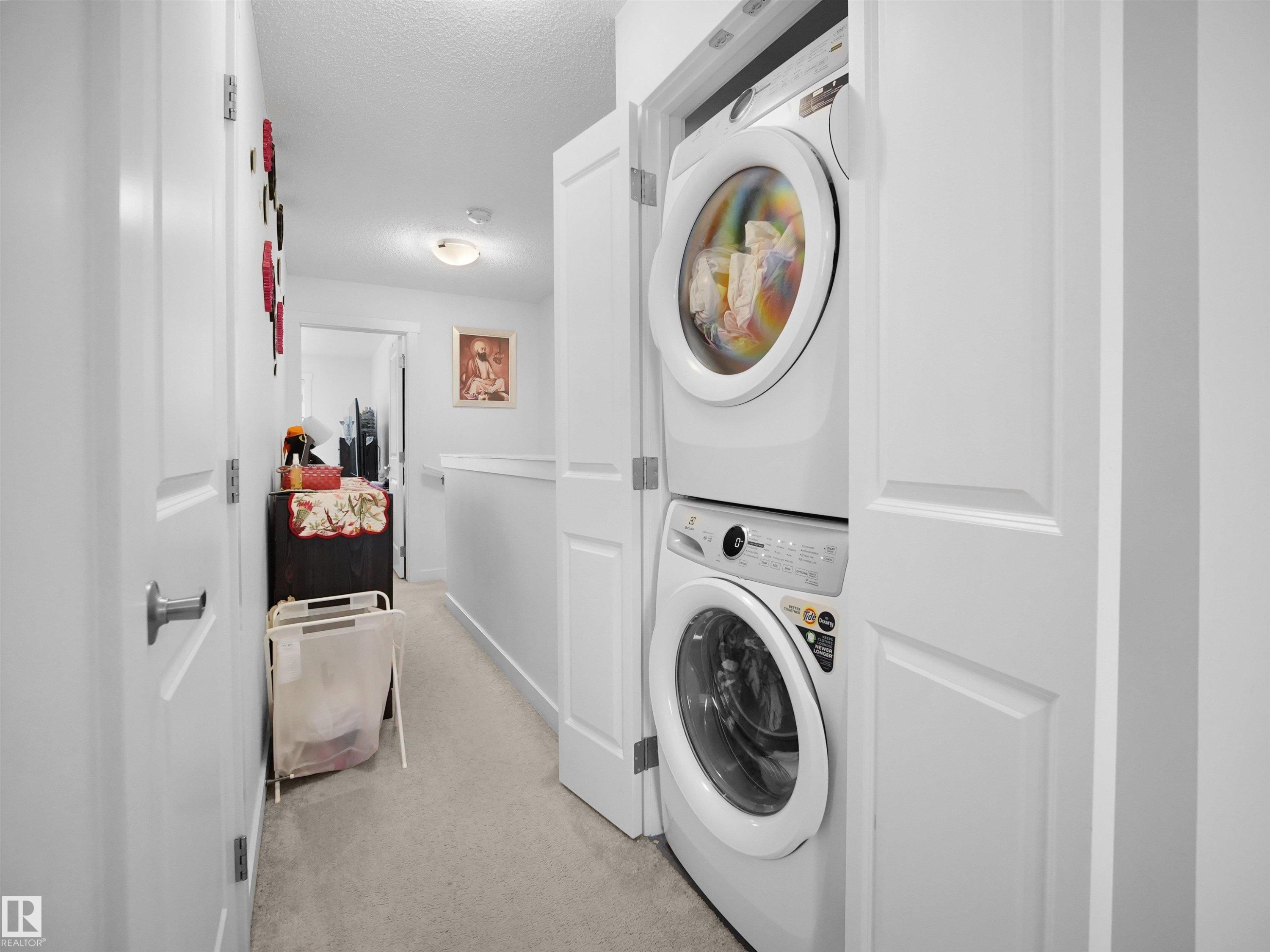 The property includes a laundry area with a stacked washer and dryer, located in a hallway with light-colored carpeting and white walls - 64 655 Watt Boulevard, Edmonton, AB - Indoor Photo Showing Laundry Room