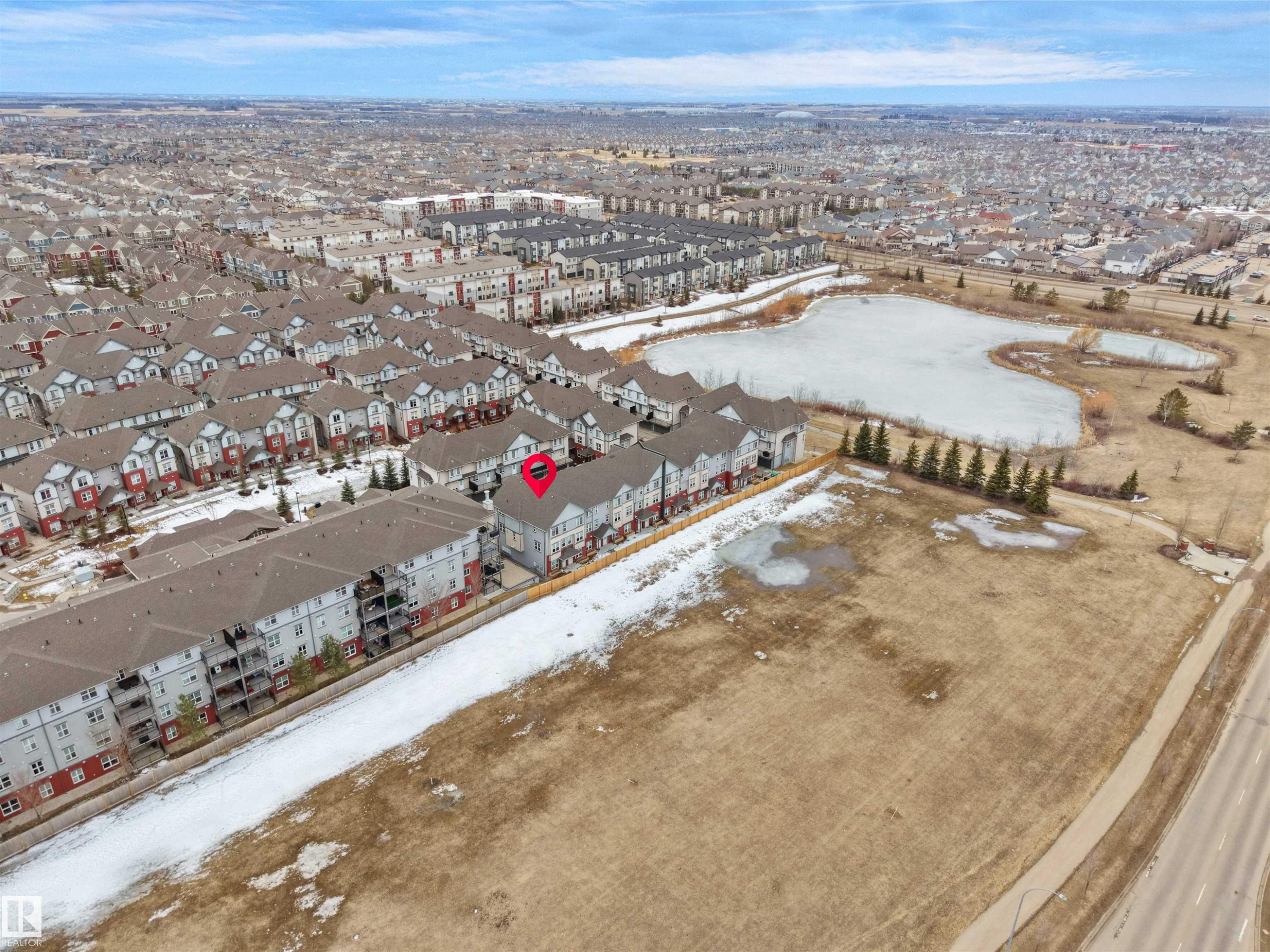 Aerial view showcasing the property within a community of residences, with a frozen pond and mature trees visible in the general vicinity - 64 655 Watt Boulevard, Edmonton, AB - Outdoor With View