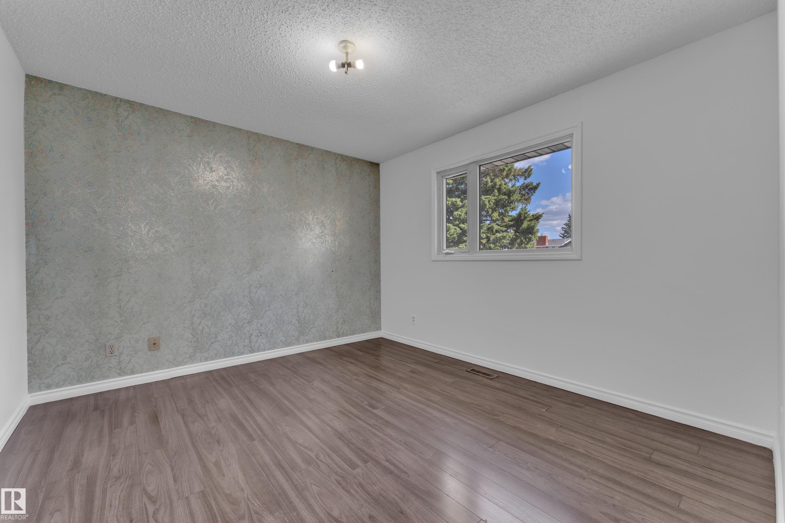 Room featuring wood-finish flooring, a textured accent wall, white baseboards, and a window with white trim - 3520 19 Avenue, Edmonton, AB