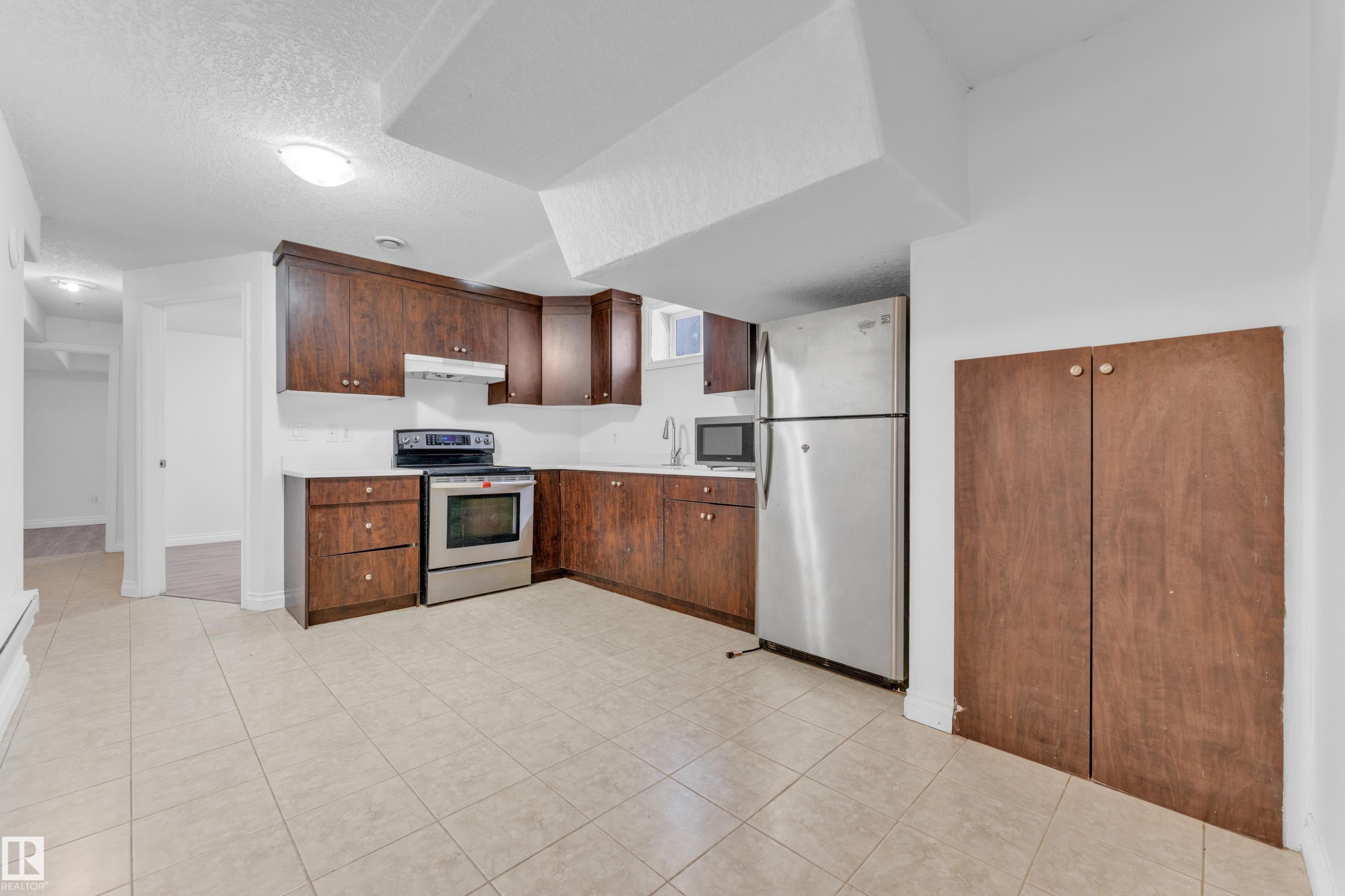 Kitchen featuring dark wood cabinetry, stainless steel appliances, light-toned countertops, and ceramic tile flooring - 3520 19 Avenue, Edmonton, AB