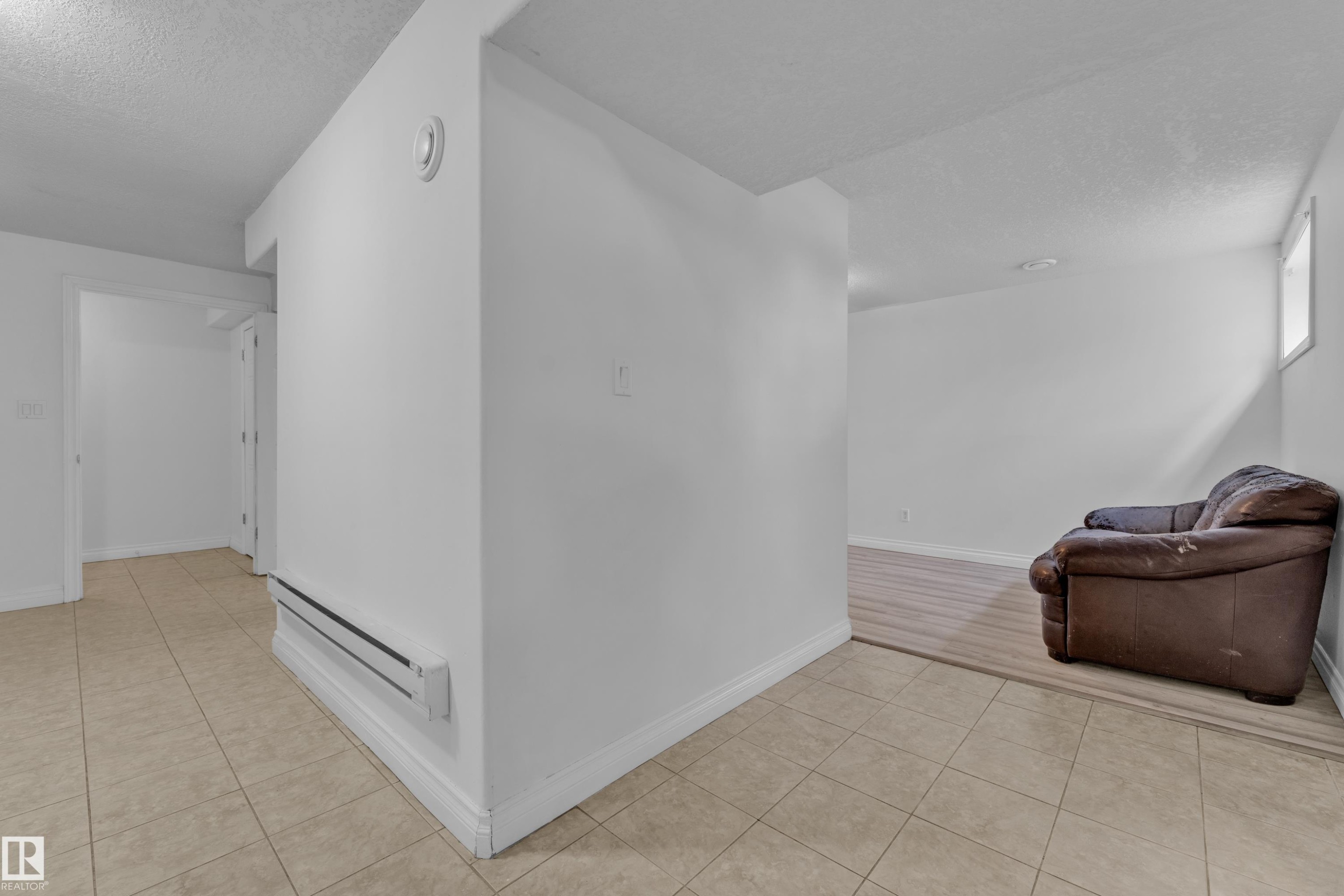 Spacious lower-level area featuring light-toned tile flooring in the foreground and wood-finish flooring in the background - 3520 19 Avenue, Edmonton, AB
