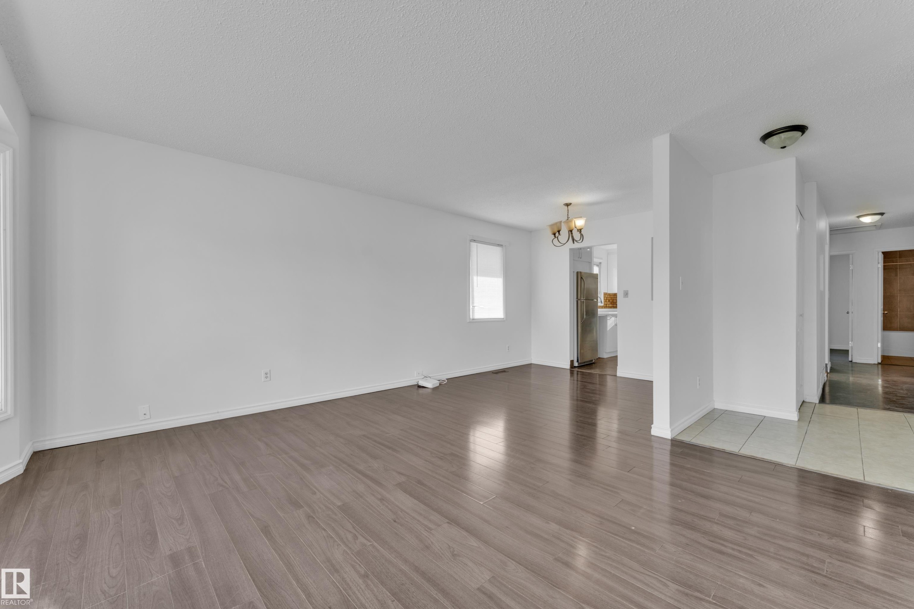 Spacious room featuring wood-finish flooring, white painted walls, and natural light from multiple windows - 3520 19 Avenue, Edmonton, AB