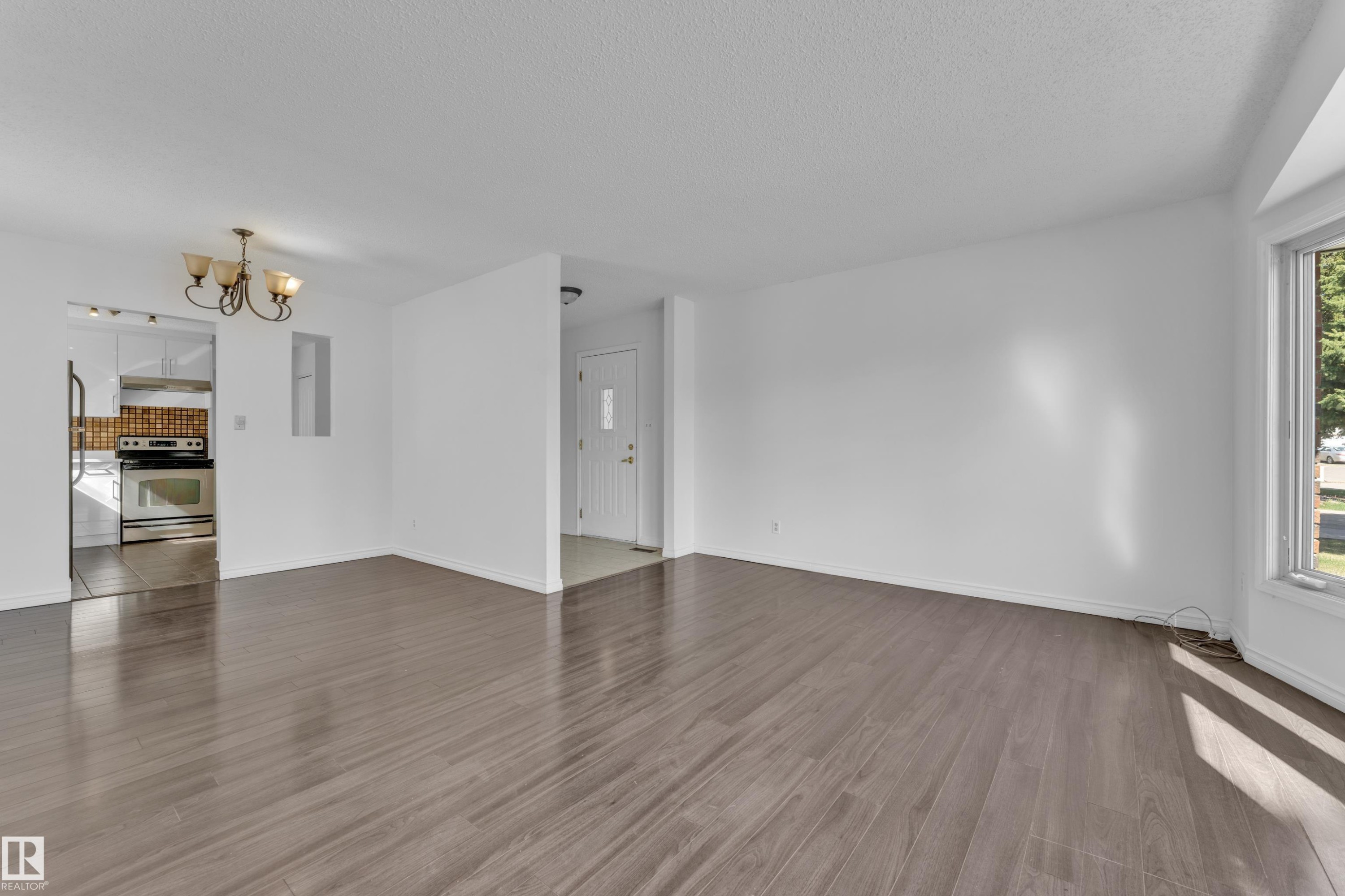 Spacious room featuring wood-finish flooring, white walls, and a large window providing natural light - 3520 19 Avenue, Edmonton, AB