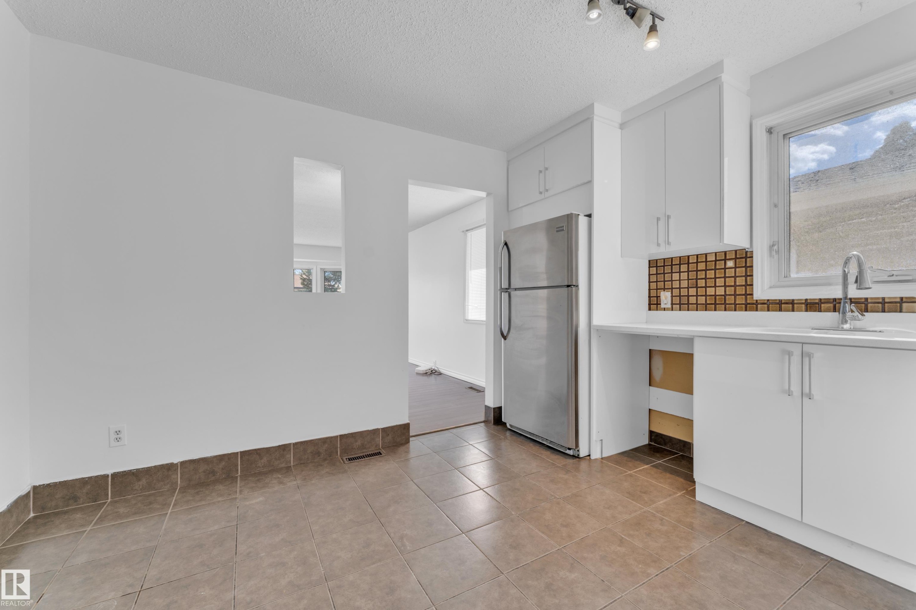 Bright kitchen area featuring white cabinetry, a stainless steel refrigerator, white countertops, a mosaic tile backsplash, and a window above the sink - 3520 19 Avenue, Edmonton, AB