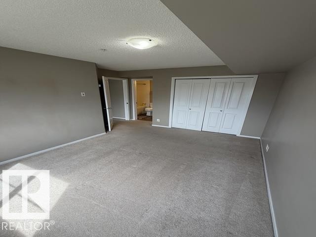 Spacious carpeted room featuring a ceiling-mounted light fixture, neutral wall colors, white baseboards, and a white bi-fold closet door - 321 107 Watt Common, Edmonton, AB - Indoor Photo Showing Other Room