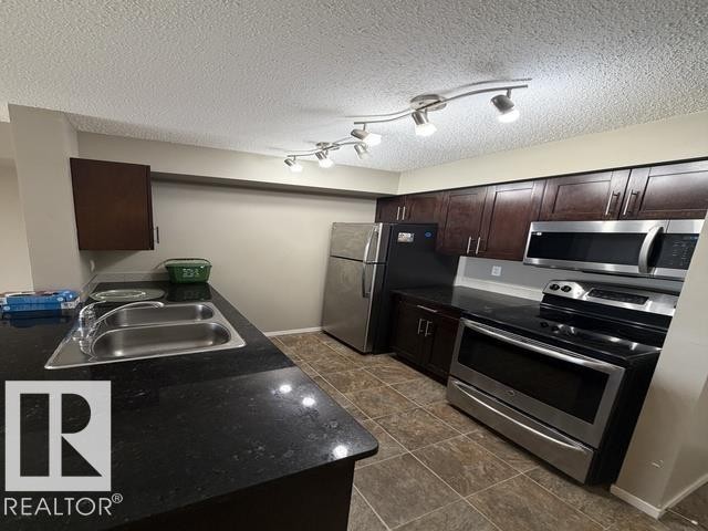 Kitchen featuring dark wood-finish cabinetry, black countertops, and stainless steel appliances - 321 107 Watt Common, Edmonton, AB - Indoor Photo Showing Kitchen With Double Sink