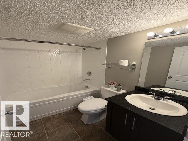 Full bathroom with a white tub and shower surround, dark brown floor tiles, and a dark wood-finish vanity with a light-colored countertop - 321 107 Watt Common, Edmonton, AB - Indoor Photo Showing Bathroom