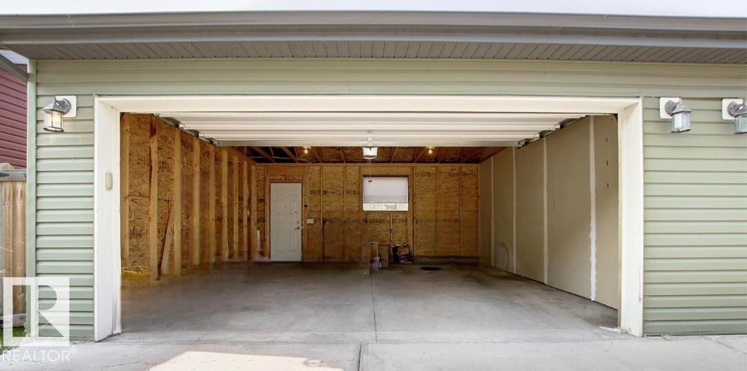 Spacious garage with an open overhead door, featuring concrete flooring, interior framing, and a utility door - 225 51A Street Sw, Edmonton, AB
