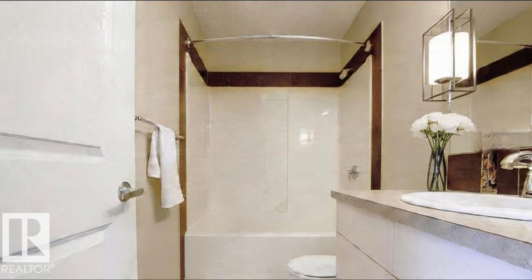 Bathroom featuring a white vanity with an integrated sink, polished chrome faucet, and a contemporary pendant light fixture - 225 51A Street Sw, Edmonton, AB