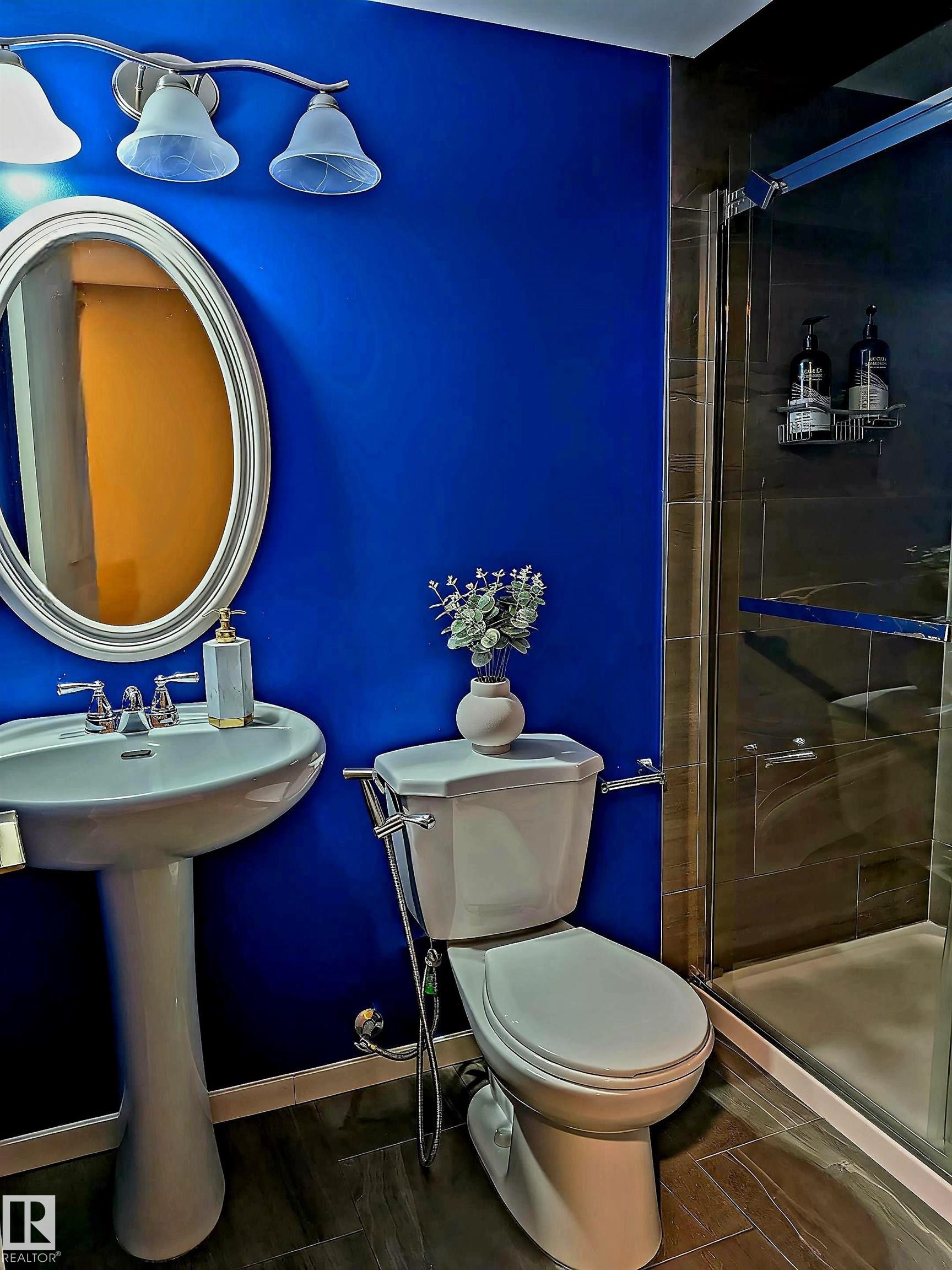Pedestal sink with chrome faucet, an oval mirror, and a three-light vanity fixture - 225 51A Street Sw, Edmonton, AB
