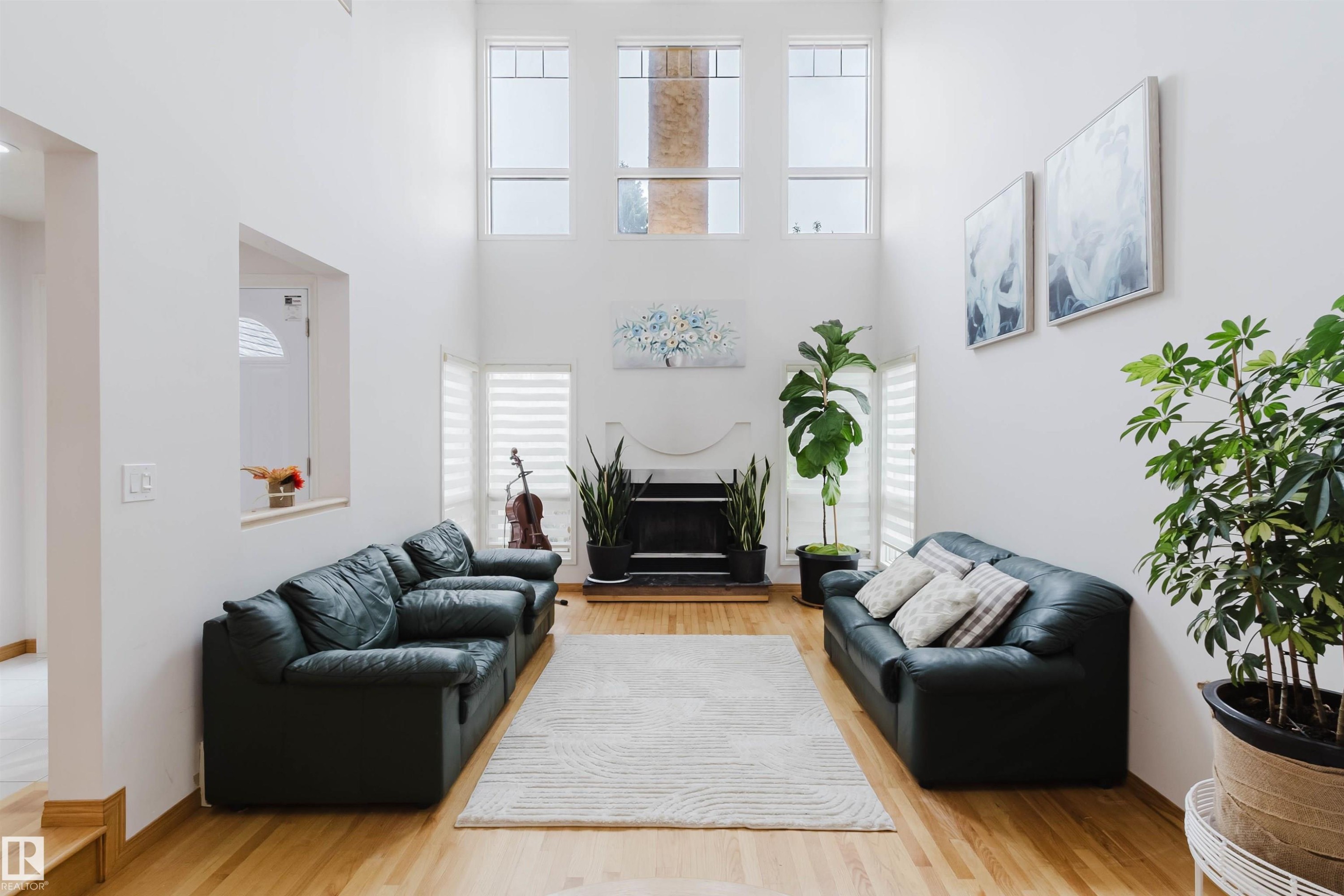Two-story living area featuring a central fireplace with mantel, high ceilings, multiple windows, and wood-finish flooring - 342 O'Connor Close, Edmonton, AB - Indoor Photo Showing Living Room With Fireplace