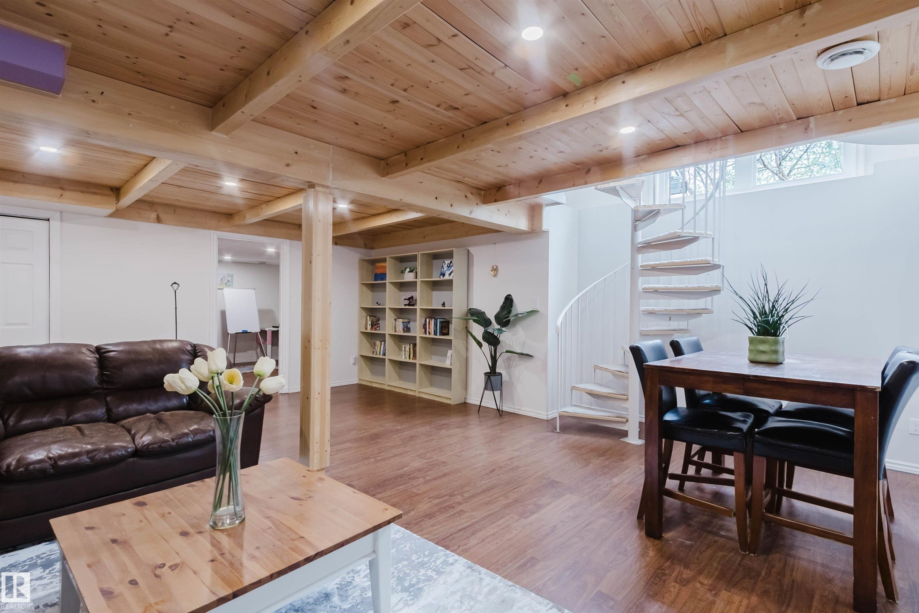 Lower level living area featuring a spiral staircase, wood-finish flooring, exposed wood beam ceiling, and built-in shelving - 342 O'Connor Close, Edmonton, AB - Indoor