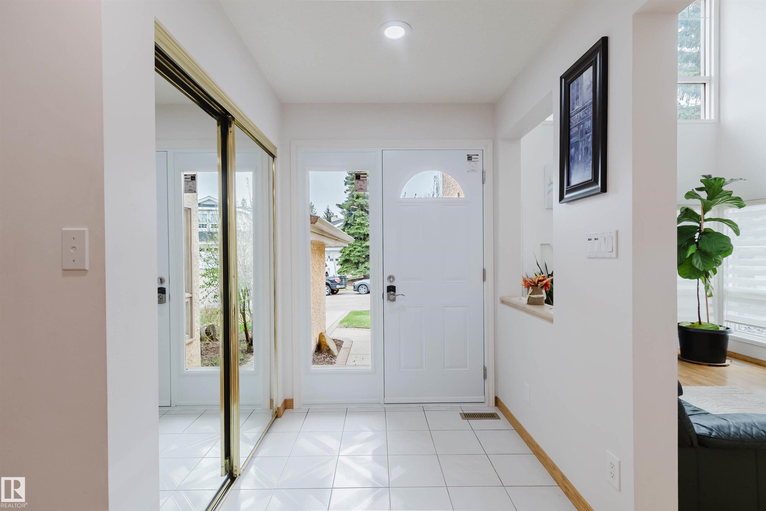 Bright entryway featuring white tiled flooring, a white front door with a decorative half-moon window, an adjacent sidelight window, and a built-in mirrored closet with brass-finish trim - 342 O'Connor Close, Edmonton, AB - Indoor Photo Showing Other Room