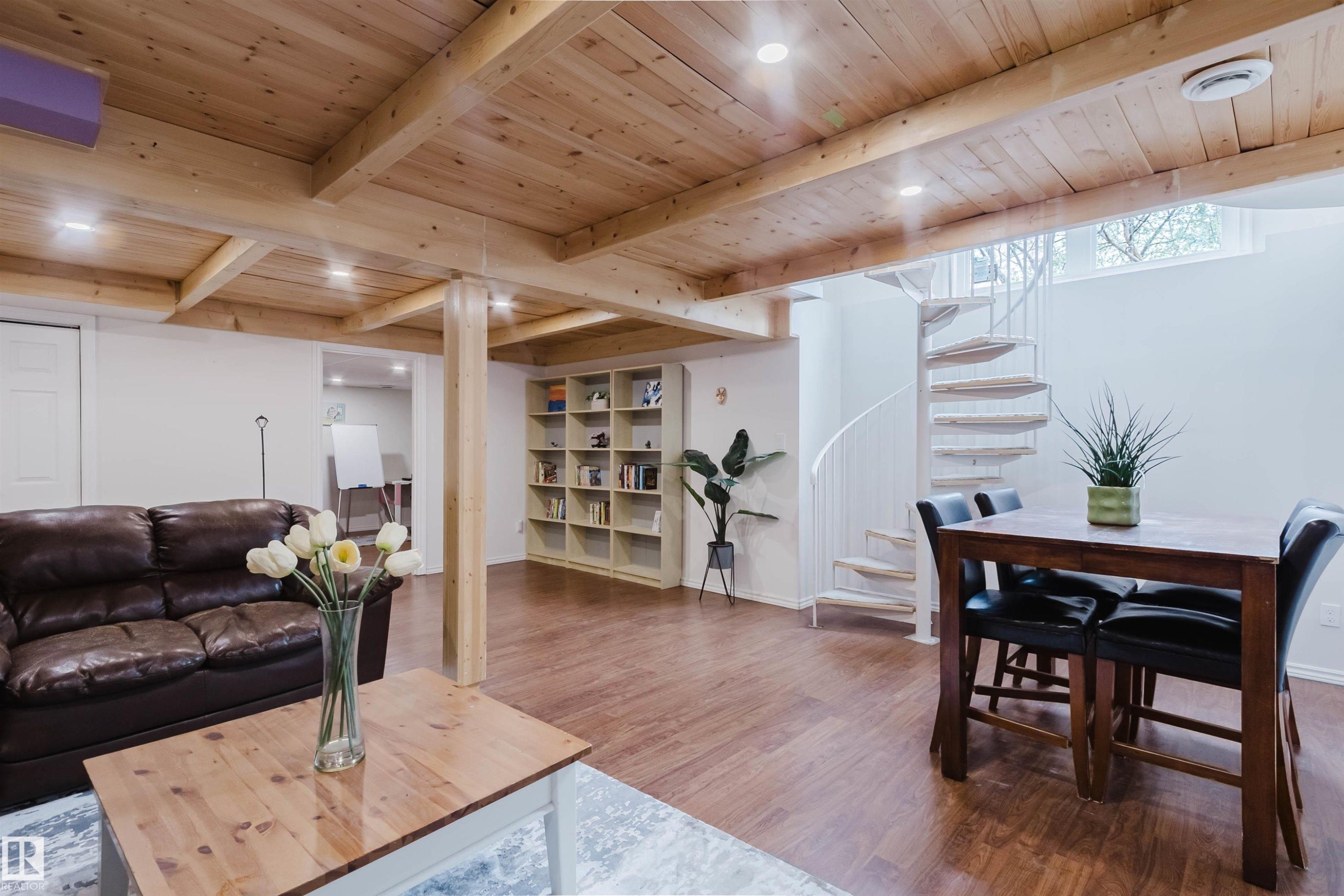 Open-concept interior featuring wood-finish flooring, exposed wooden ceiling beams, recessed lighting, a white spiral staircase, and a built-in shelving unit - 342 O'Connor Close, Edmonton, AB - Indoor