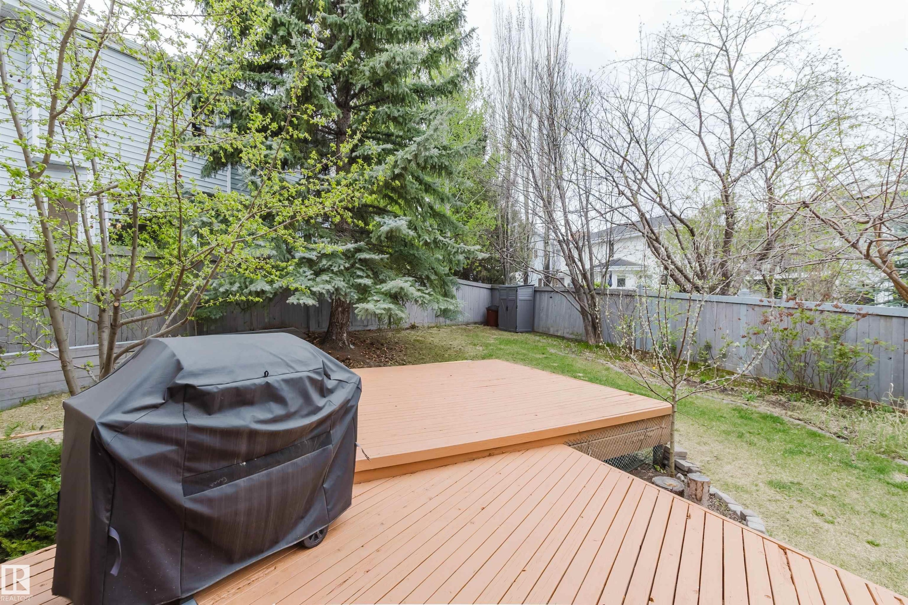 Multi-level wood deck overlooking a spacious backyard with a lawn area, mature trees, and a privacy fence - 342 O'Connor Close, Edmonton, AB - Outdoor