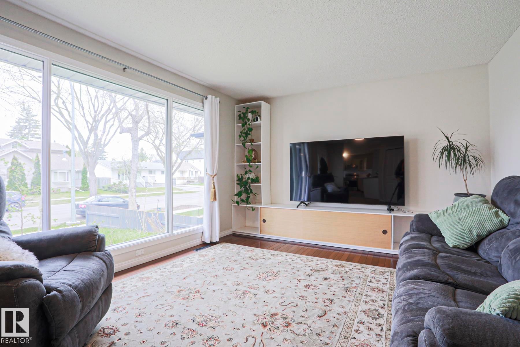 Room featuring large picture windows, wood-finish flooring, and a built-in media console with open shelving - 9523 151 Street, Edmonton, AB - Indoor Photo Showing Living Room