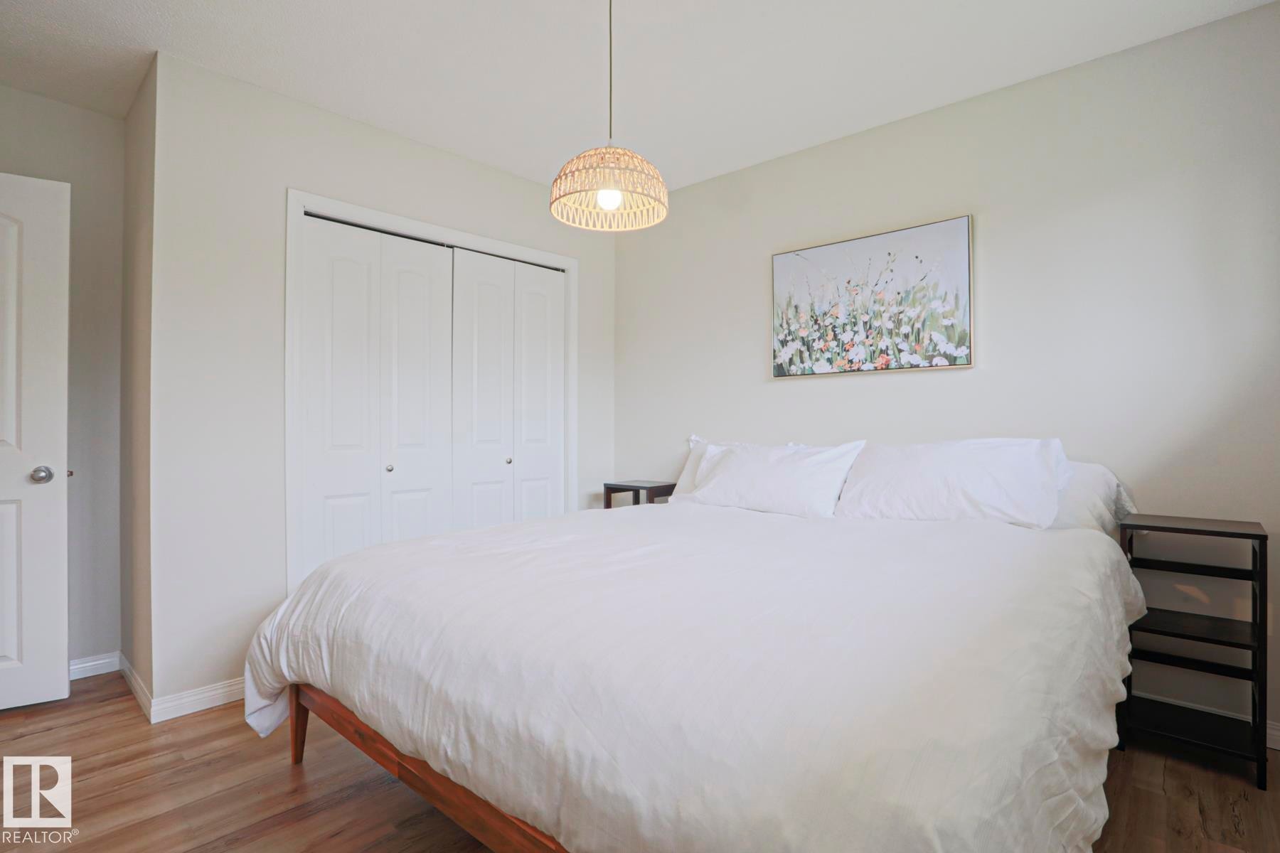 Bedroom featuring light-toned walls, wood-finish flooring, a built-in closet with bifold doors, and a woven pendant light fixture - 9523 151 Street, Edmonton, AB - Indoor Photo Showing Bedroom