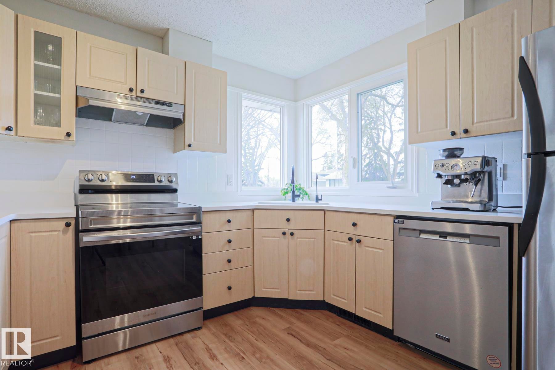 Kitchen featuring light-toned cabinetry, stainless steel appliances, and wood-finish flooring - 9523 151 Street, Edmonton, AB - Indoor Photo Showing Kitchen