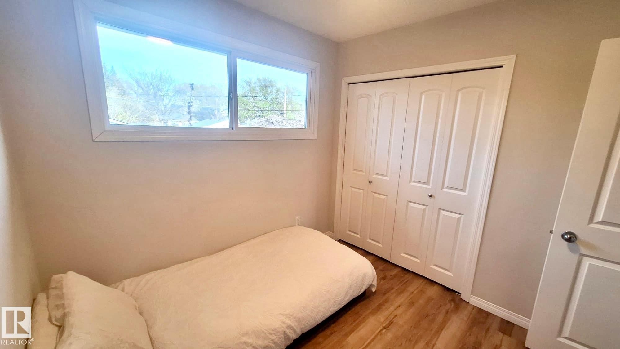 Bright room with a large window, neutral wall paint, wood-finish flooring, and bi-fold closet doors - 9523 151 Street, Edmonton, AB - Indoor Photo Showing Bedroom