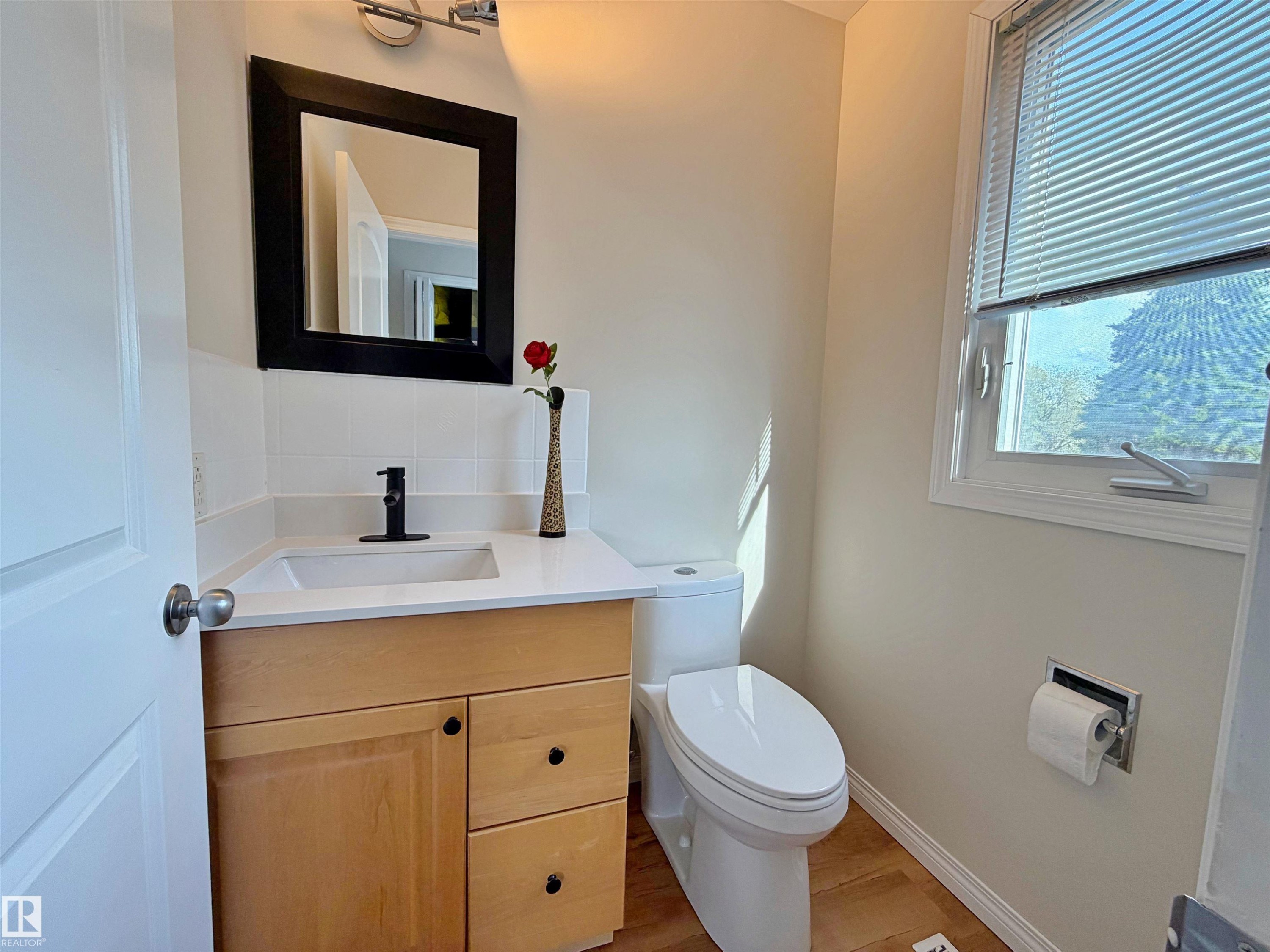 Bathroom featuring a light wood-finish vanity with a white countertop and integrated sink, matte black faucet, and a rectangular black-framed mirror - 9523 151 Street, Edmonton, AB - Indoor Photo Showing Bathroom