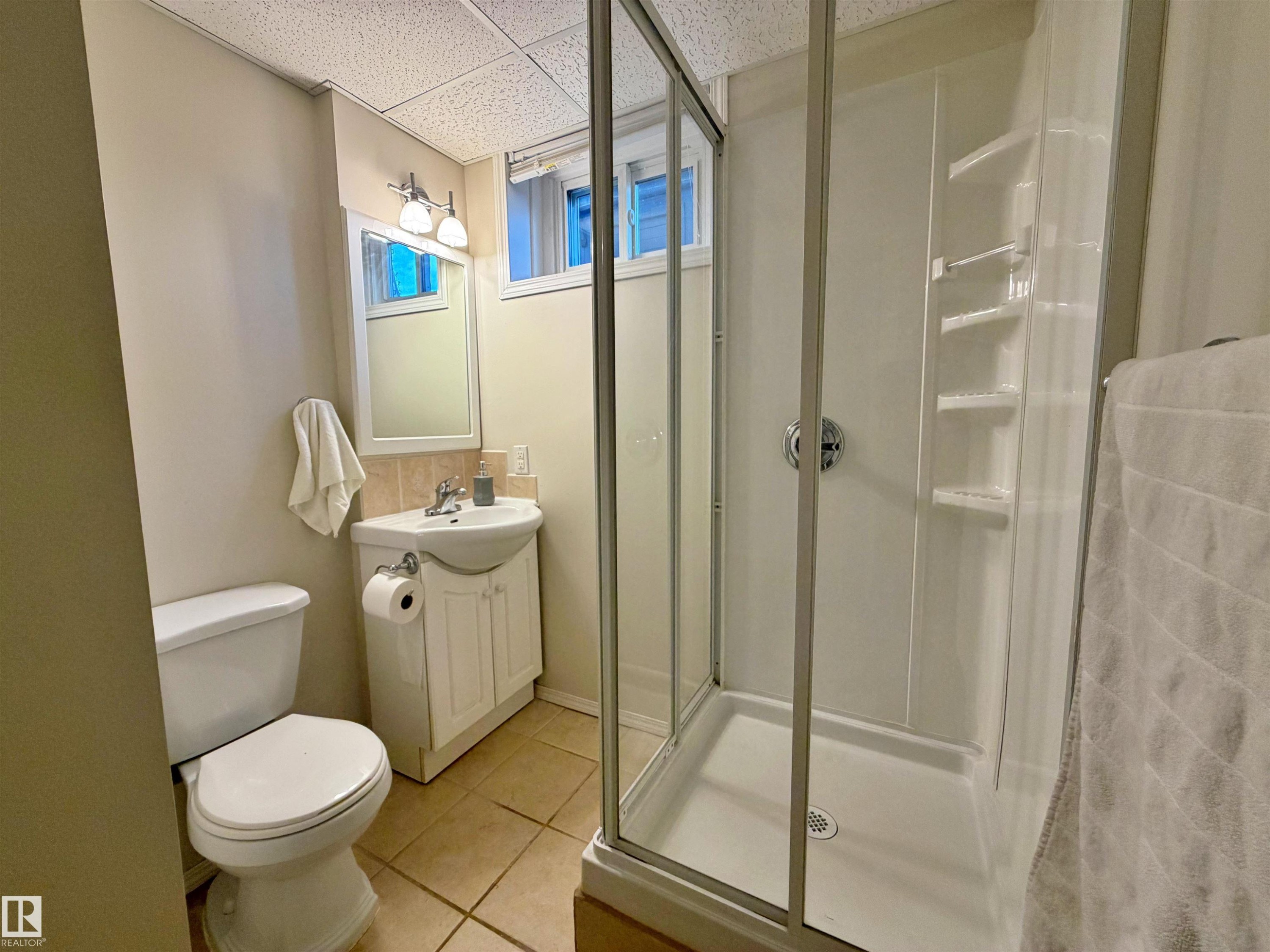 Bathroom featuring a glass-enclosed shower, a white vanity with an integrated sink, a toilet, an overhead light fixture, and tiled flooring - 9523 151 Street, Edmonton, AB - Indoor Photo Showing Bathroom