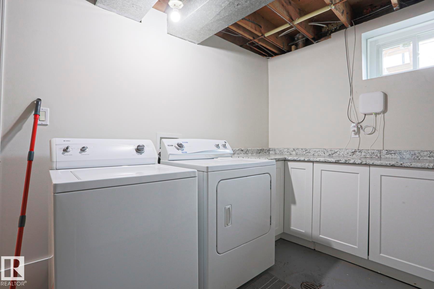 Laundry area featuring white cabinetry, a speckled countertop, and a window providing natural light - 9523 151 Street, Edmonton, AB - Indoor Photo Showing Laundry Room