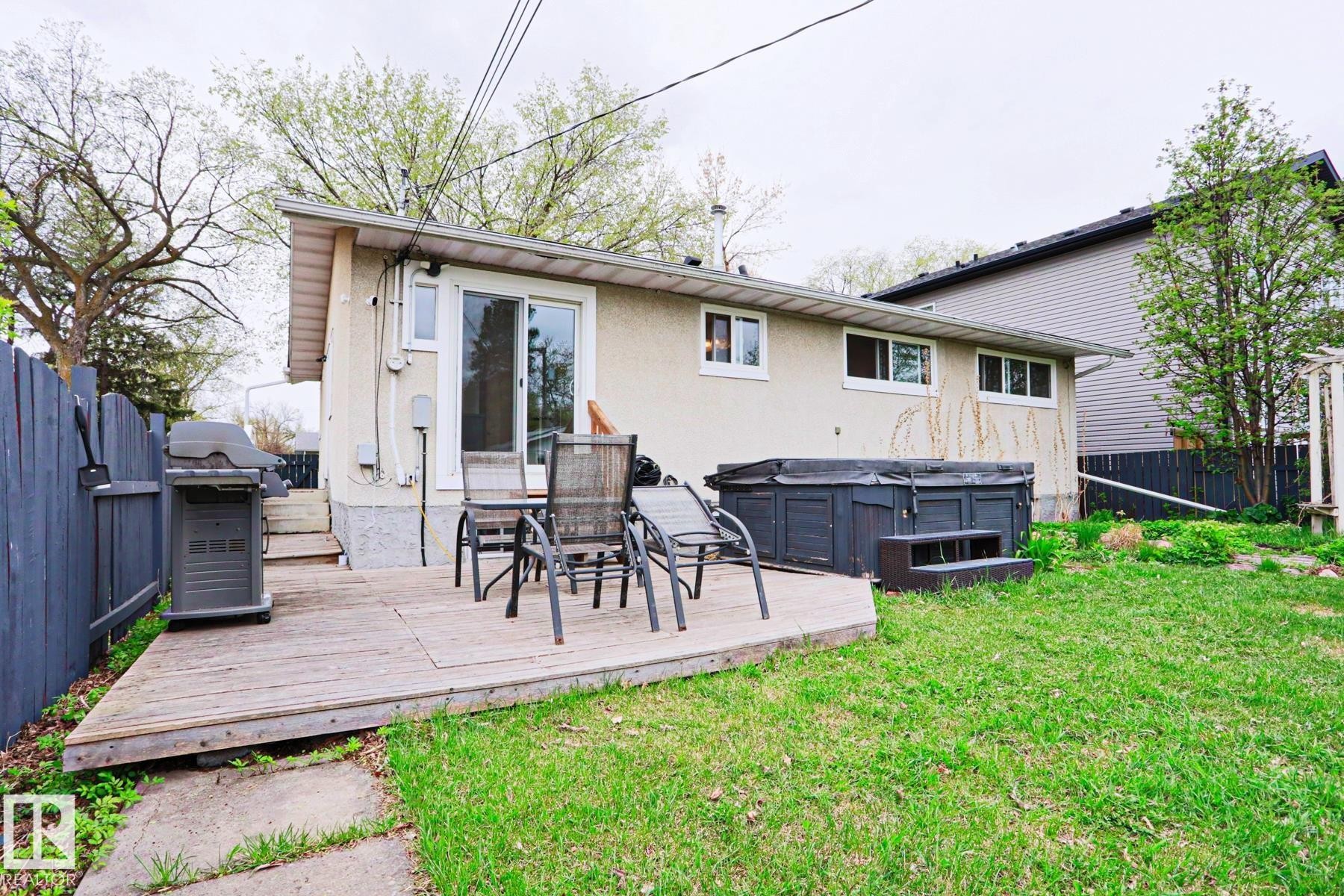 Rear exterior showcasing a wooden deck, a hot tub, and a grassy lawn - 9523 151 Street, Edmonton, AB - Outdoor With Deck Patio Veranda