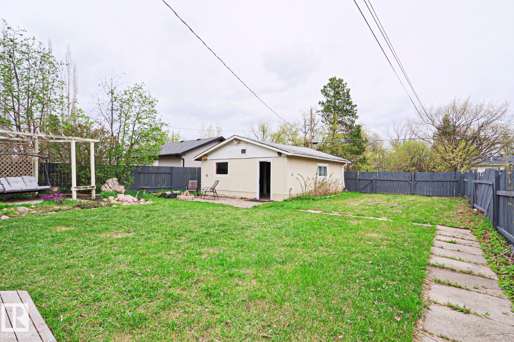 Expansive grassy yard area featuring a detached auxiliary building, perimeter fencing, a wooden pergola structure, and a concrete paver pathway - 9523 151 Street, Edmonton, AB - Outdoor With Backyard