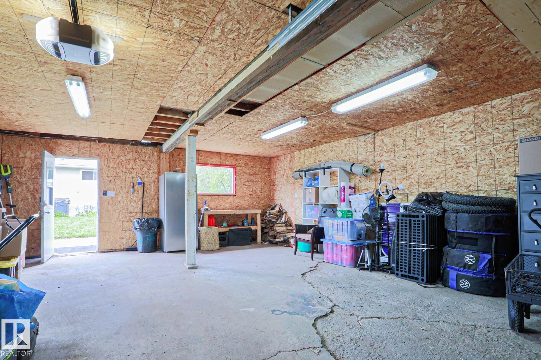 Spacious garage featuring concrete flooring, exposed OSB walls and ceiling, fluorescent lighting, a garage door opener, and an exterior access door - 9523 151 Street, Edmonton, AB - Indoor Photo Showing Garage